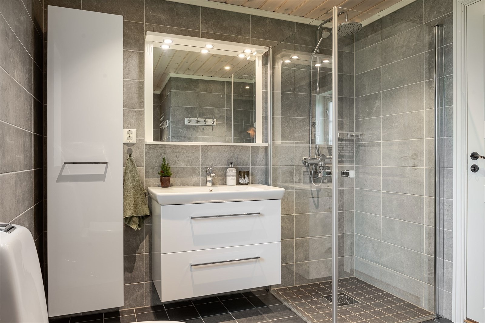 Baderommet er også utstyrt med dusjhjørne med glassdører og både hånd- og regnfallsdusj, gulvstående toalett og opplegg for vaskemaskin. Galleribilde