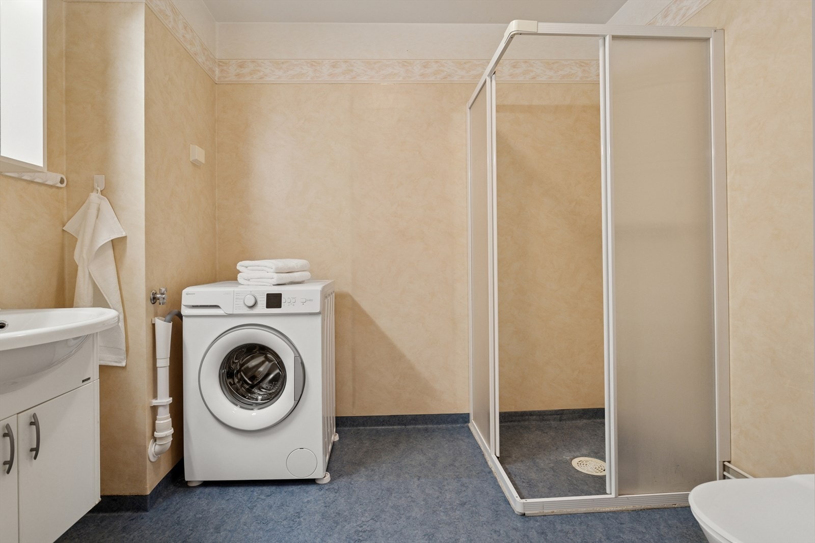 Videre et badet innredet med servant med skapplass, dusjhjørne, toalett og opplegg til vaskemaskin. Galleribilde