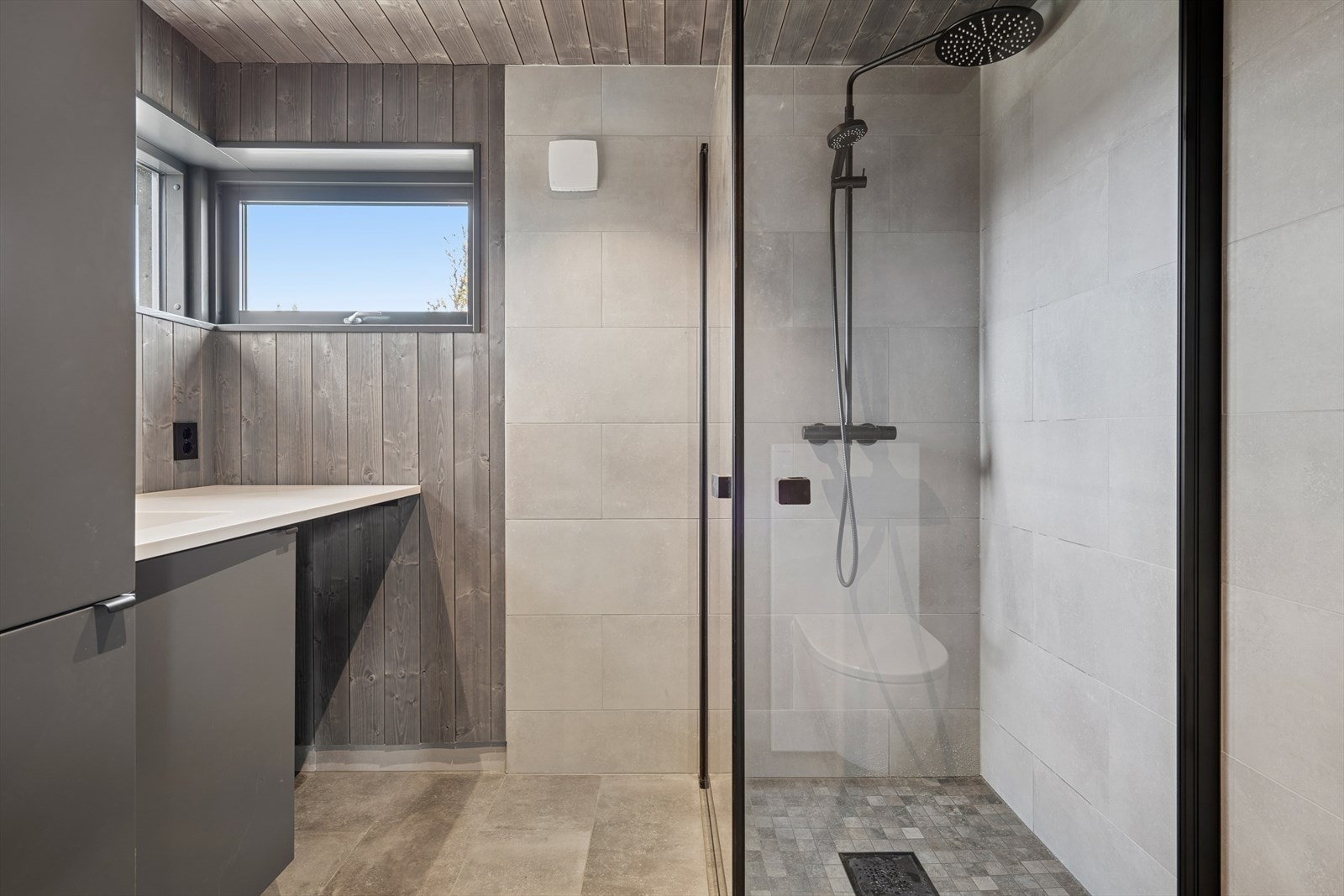 Badet har fliser på gulv med varmekabler. Dusj, vegghengt toalett og baderomsinnredning. Galleribilde