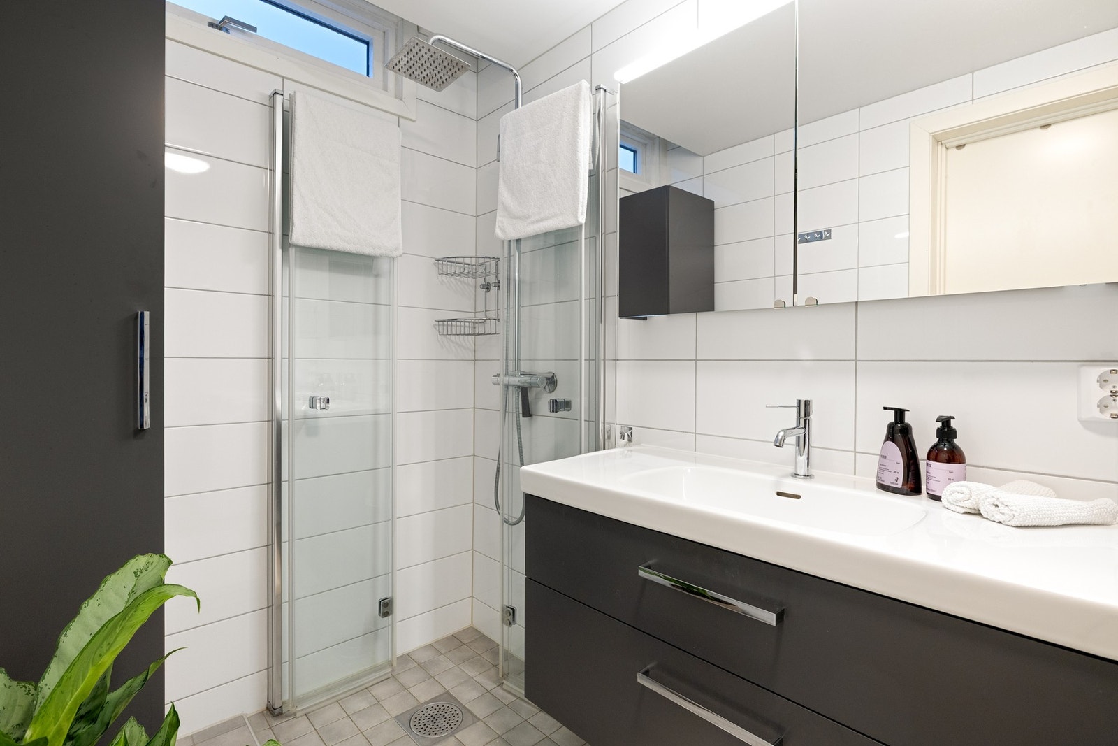 Badet har keramiske fliser på gulv og vegger og inneholder servantmøblement, vegghengt toalett, dusjhjørne og opplegg for vaskemaskin Galleribilde