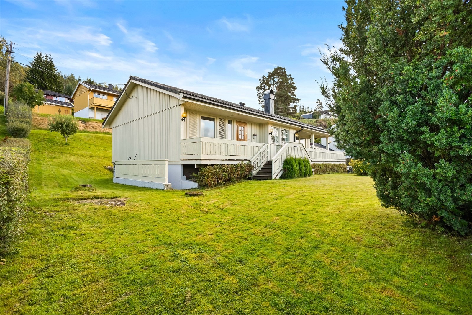 Boligen ligger på en skrånende tomt med en opparbeidet hage med plen og beplantning. Galleribilde