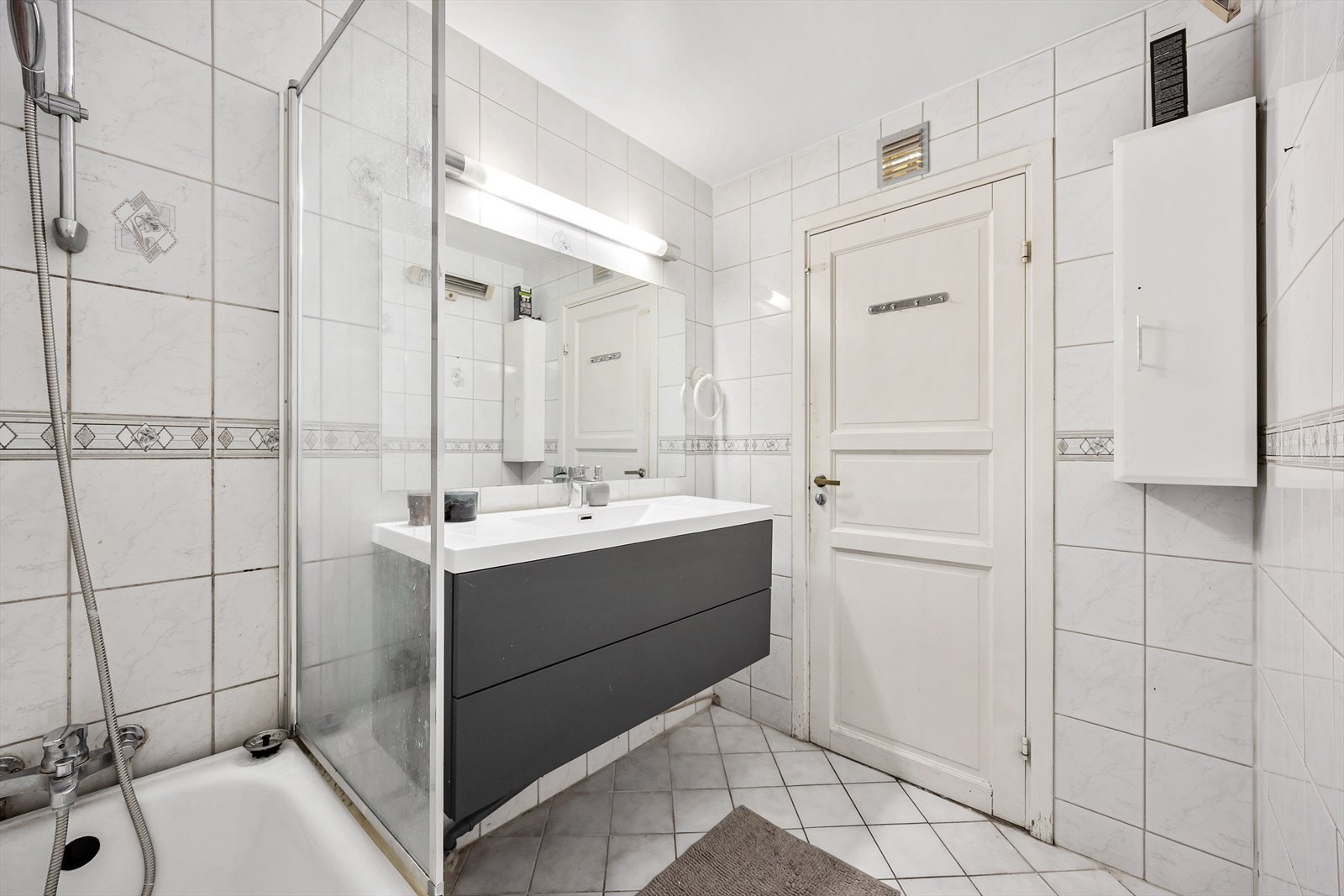 Badet består av badekar med dusjoppheng, servantseksjon med skuffer og veggmontert speil. Galleribilde