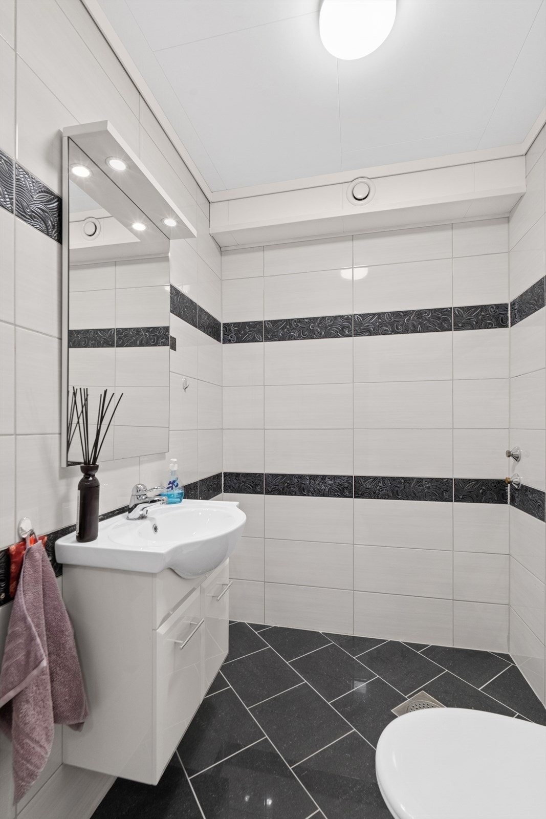 Helfliset toalettrom med toalett og servantskap, samt sluk. Mekanisk ventilert. Galleribilde