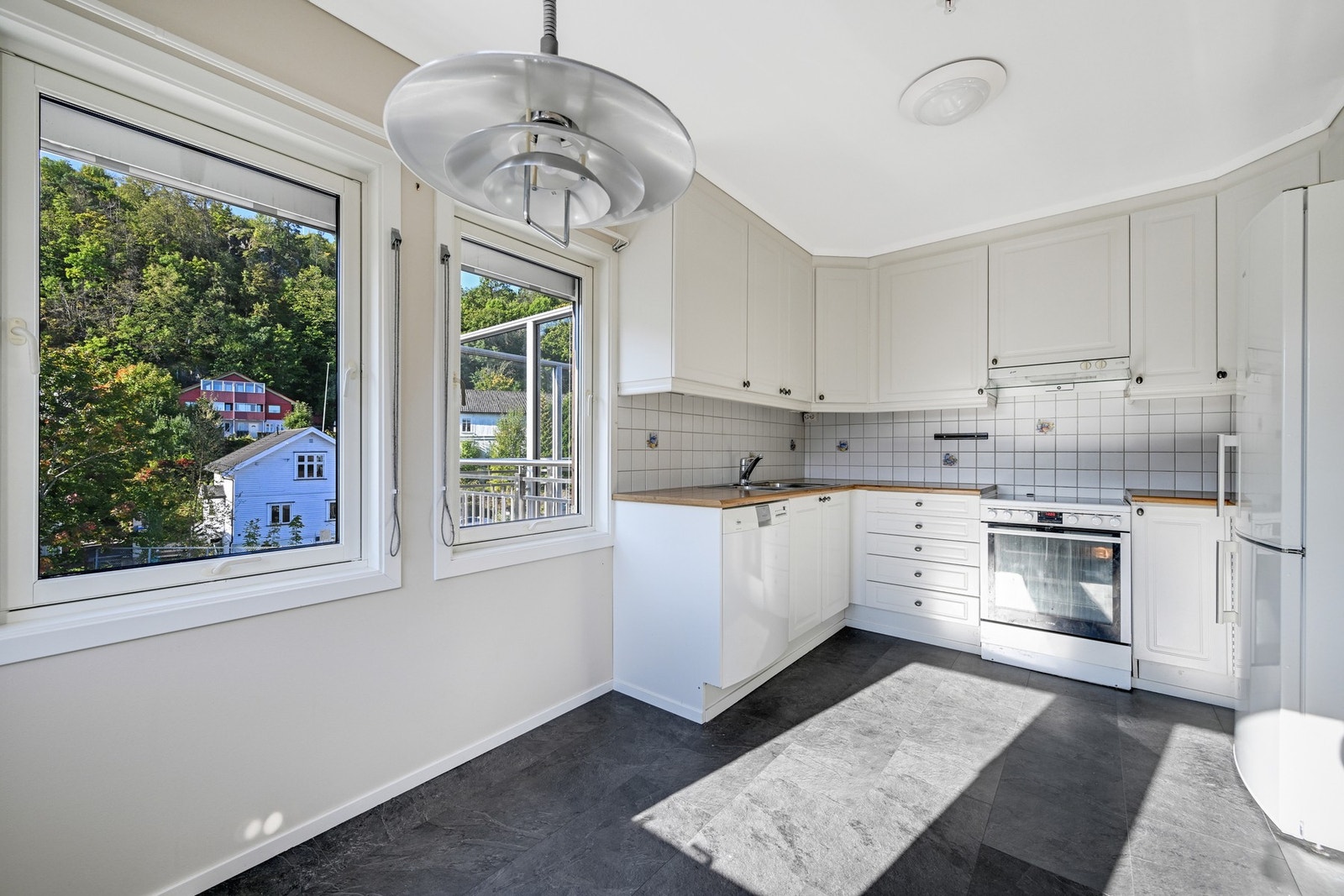 Kjøkkenet har lyse vegger, grått gulv, hvit kjøkkeninnredning og benkeplate av tre. Galleribilde