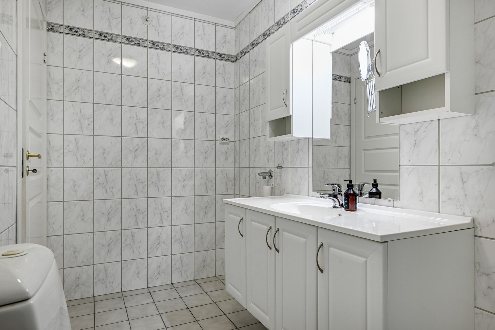 Badet har fliser på vegger og gulv, dusjkabinett, toalett og servant med underskap og speil. God plass til vaskemaskin og tørketrommel. Galleribilde