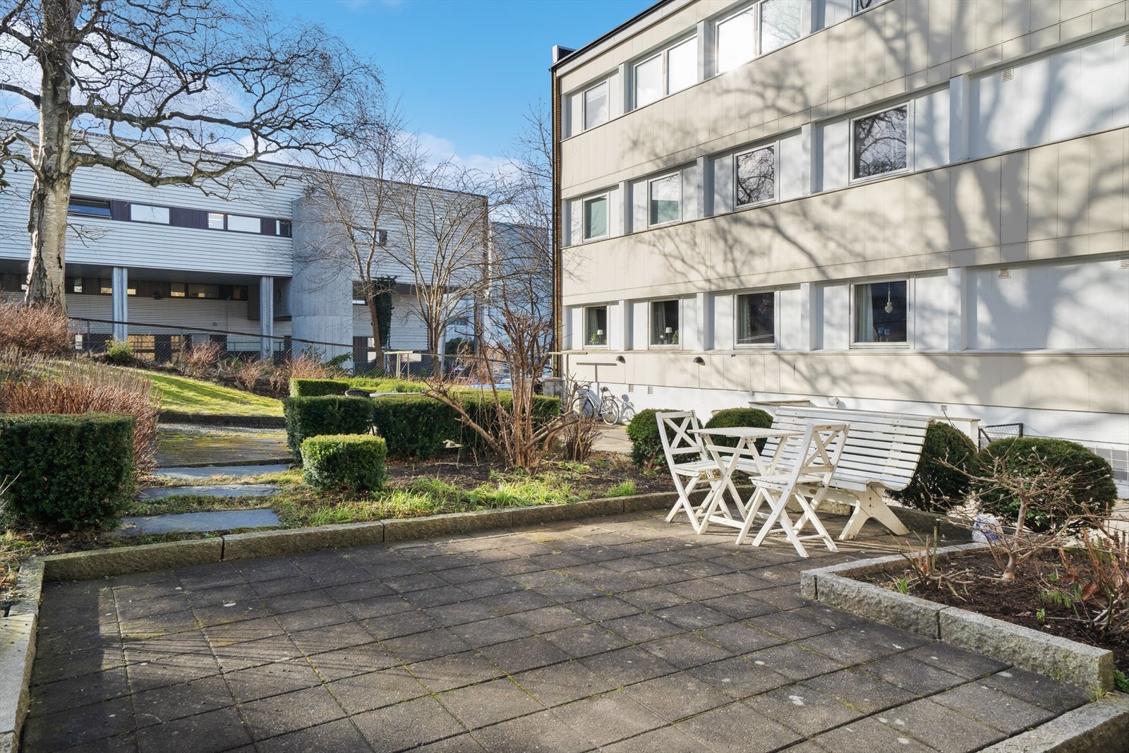 Borettslagets bakgård har steinsatte uteplasser, stier og bed som avløses av grøntareal, busker, bed, diverse beplantning og trær. Galleribilde