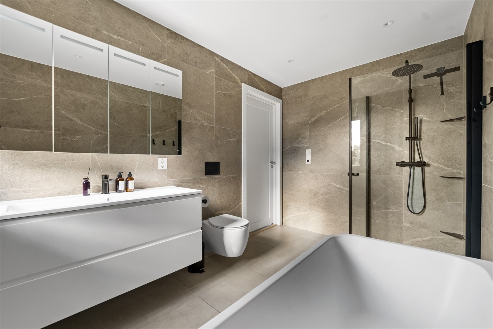 Dusjhjørne med glassdører, et topp moderne og romslig badekar og vegghengt toalett. Galleribilde