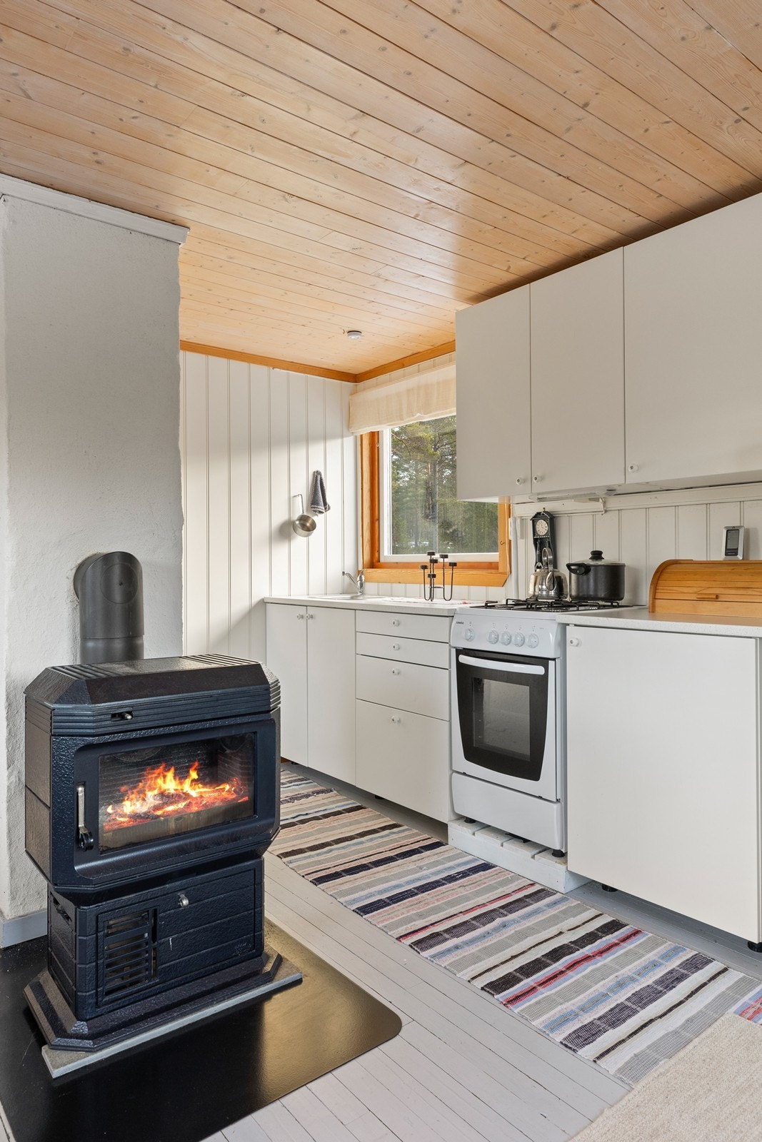 Enkelt, lyst kjøkken med frittstående komfyr og kombi kjøl/frys. Galleribilde