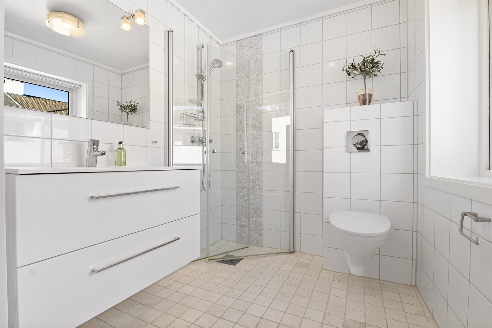 Lekkert flislagt bad med dusjsone og praktiske innfellbare dører. I tillegg er det vegghengt toalett og stilrent baderomsmøbel. Alt i lyse og moderne materialer Galleribilde