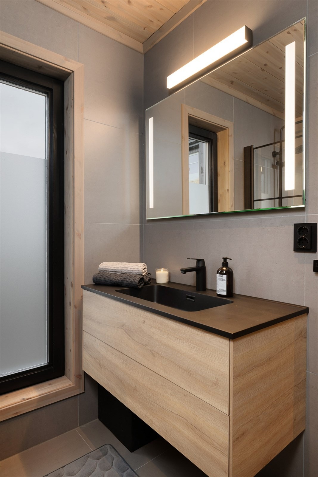 Badet er utstyrt med innredning med nedfelt servant, veggmontert toalett og dusjvegger/hjørne. Gjennomgående sorte detaljer skaper et helhetlig og moderne bad. Galleribilde