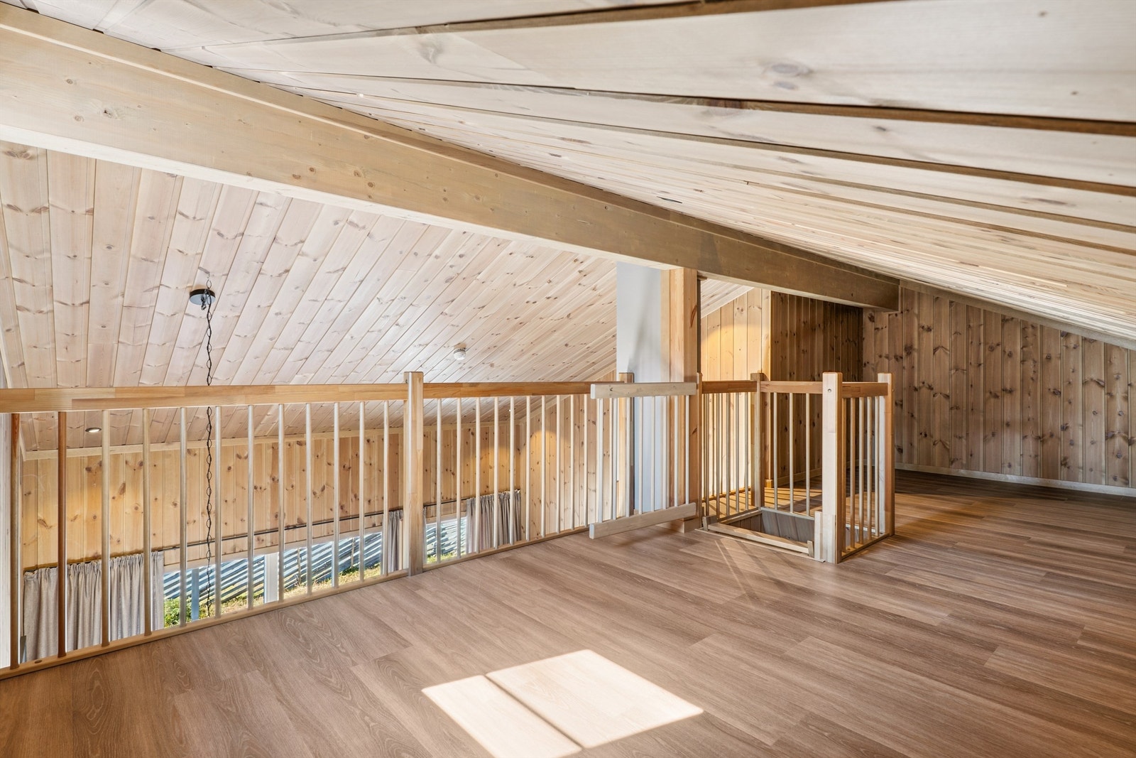 Oppe på hemsen finner du et åpent rom med panelkledde skråhimlinger og downlights. Galleribilde