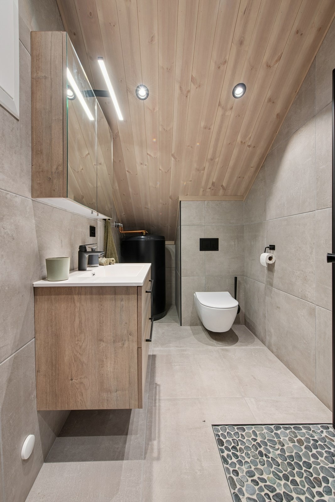 Badet i andre etasje er ekstra påkostet med fliser på både vegger og gulv. Her finner du dusj med glassdører, veggmontert toalett, romslig baderomsinnredning og varmtvannstank - en praktisk og gjennomtenkt løsning. Galleribilde