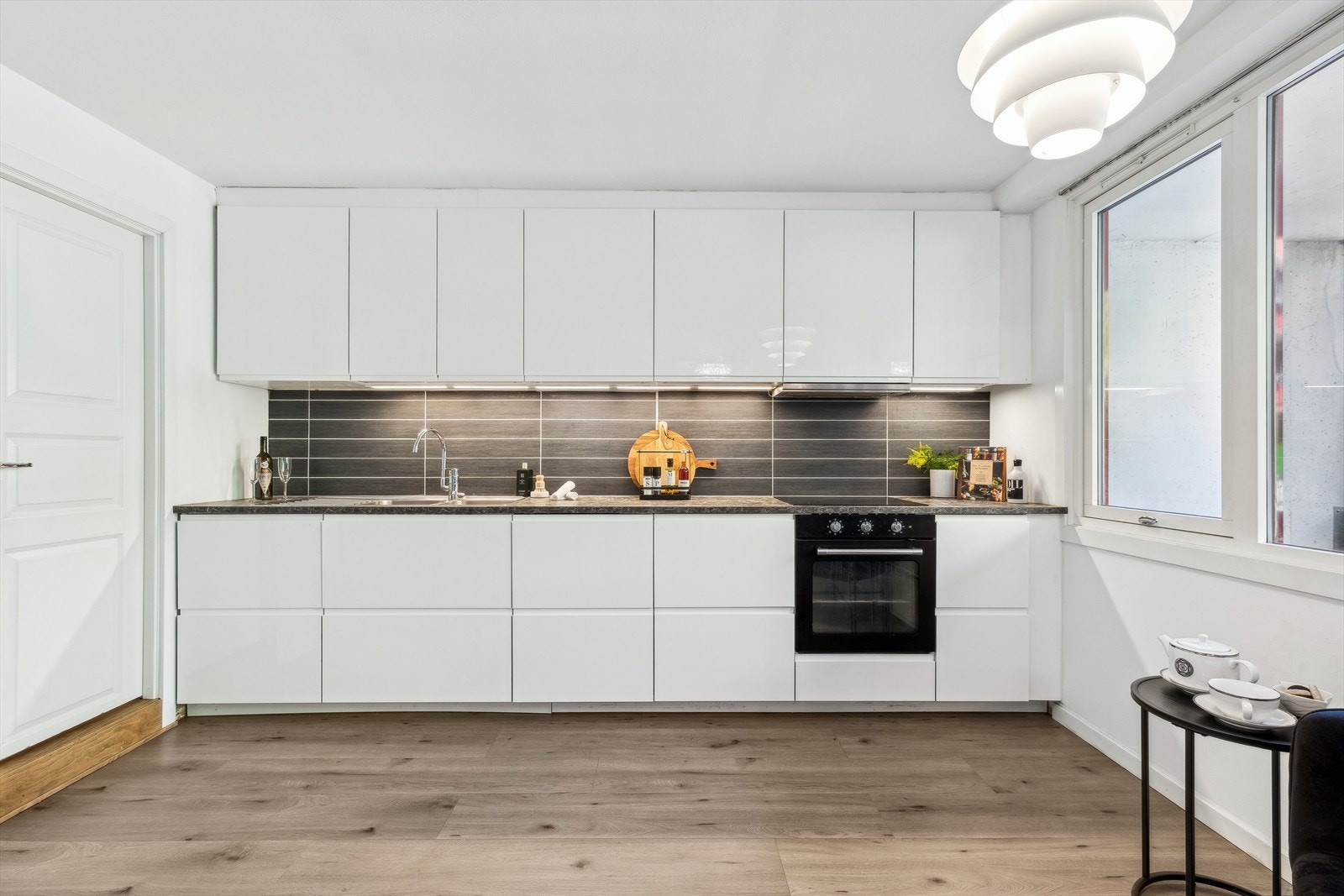 Kjøkkeninnredning med hvite høyglansede fronter. Laminat benkeplate med skyllekum og ettgreps blandebatteri. Fliser over kjøkkenbenken. Belysning under overskap. Galleribilde