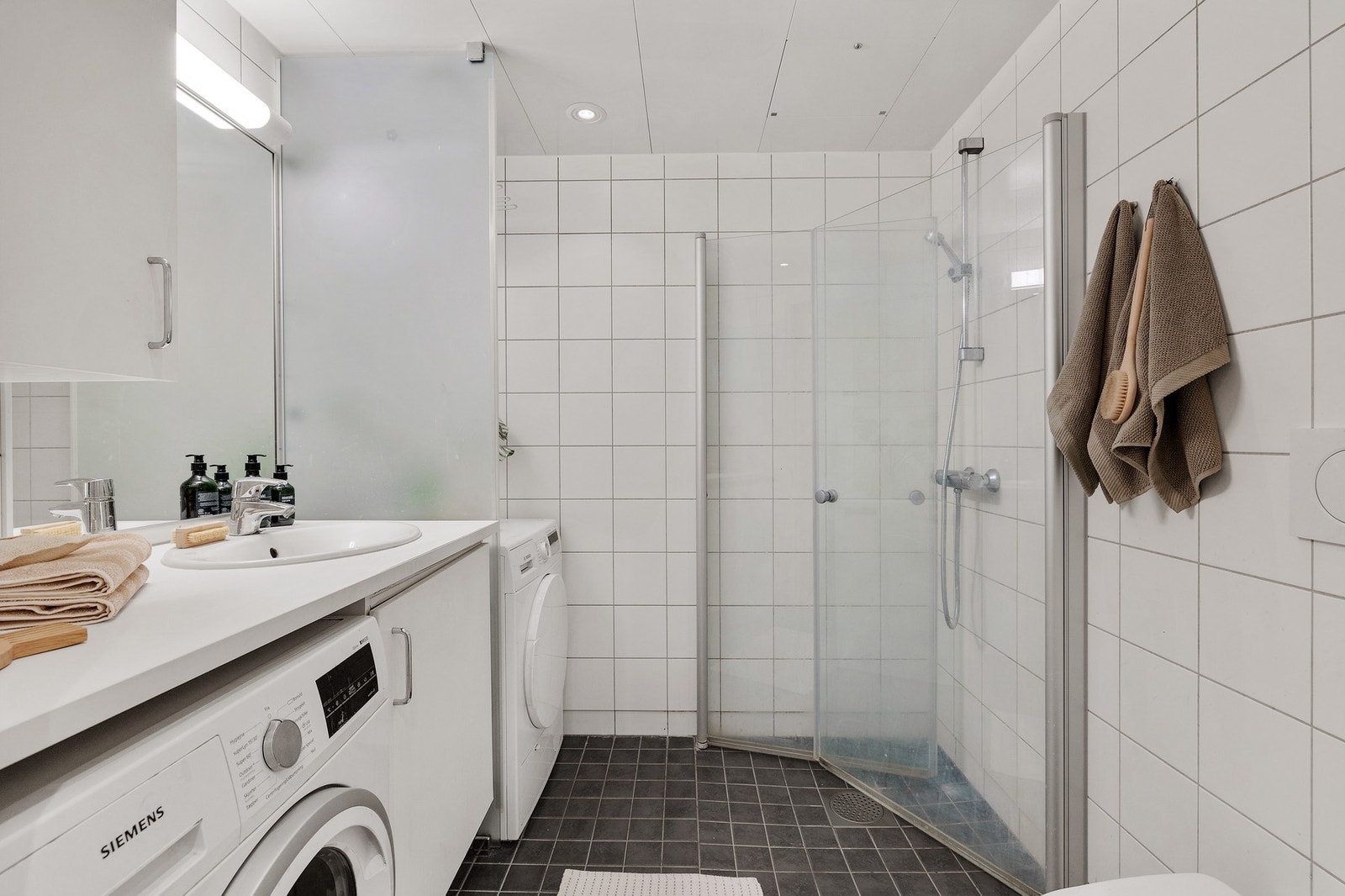 Badet er fra byggeår og er av god størrelse. Innfellbare dusjdører, opplegg til vaskemaskin, laminat benkeplate, underskap og overskap, speil og veggmontert toalett. Galleribilde