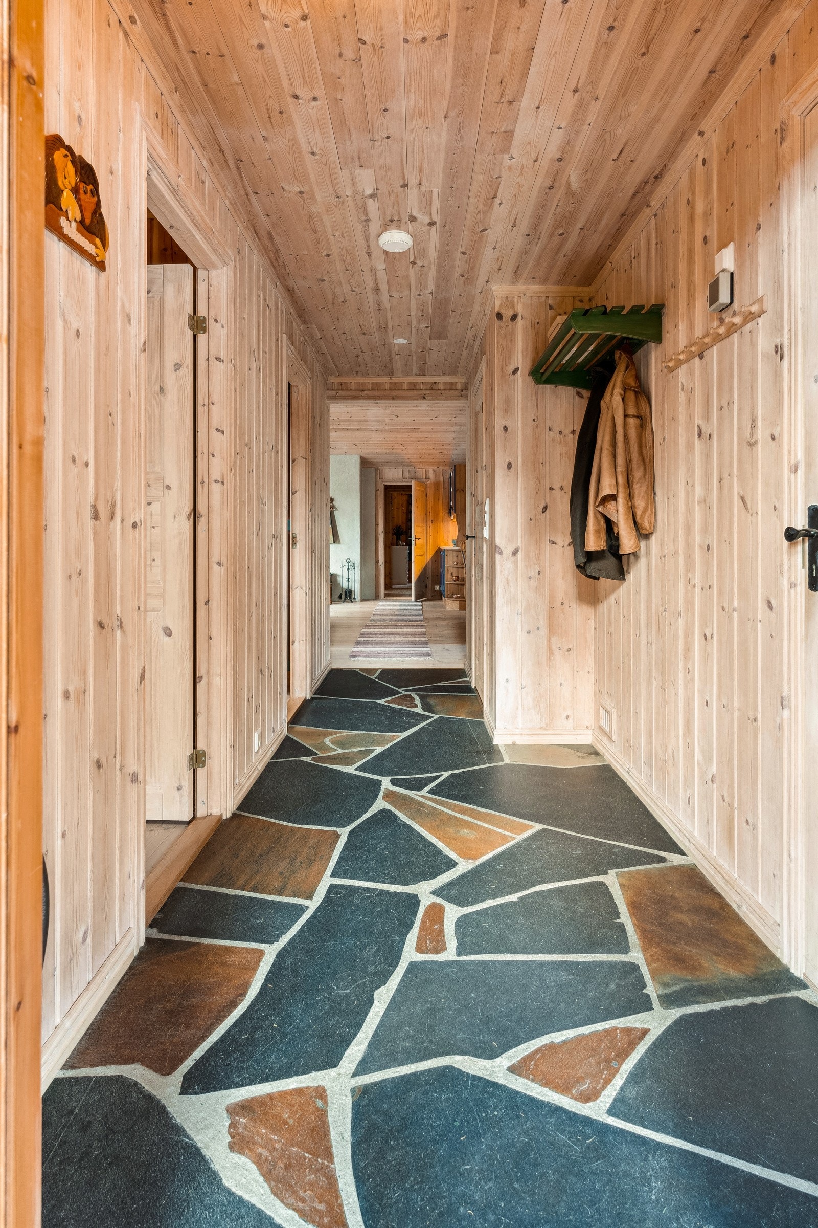 Du blir ønsket velkommen inn i en innbydende og romslig entré, hvor det er god plass til å henge fra seg yttertøy og plassering av sko. Det er lagt skifer på gulvet, og taket og veggene er kledd med panel. Galleribilde