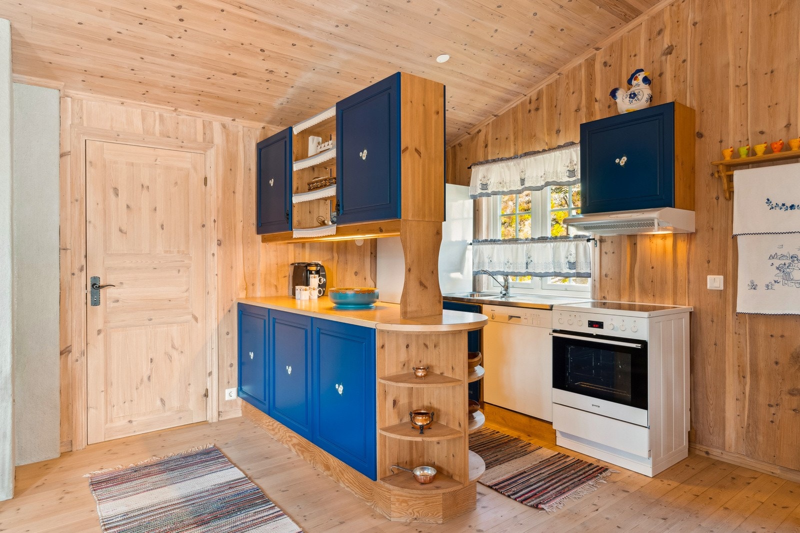 Kjøkkenet er plassert i det ene hjørnet av rommet, og er innredet med profilerte fronter i heltre, og en solid benkeplate som består av delvis heldekkende beslag og delvis laminat. Galleribilde