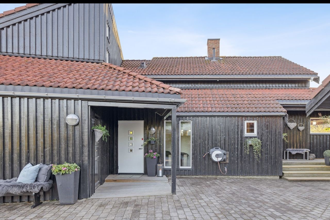 Boligen og garasjen fremstår helhetlig og velholdt med mørk bordkledning og takstein i betong Galleribilde