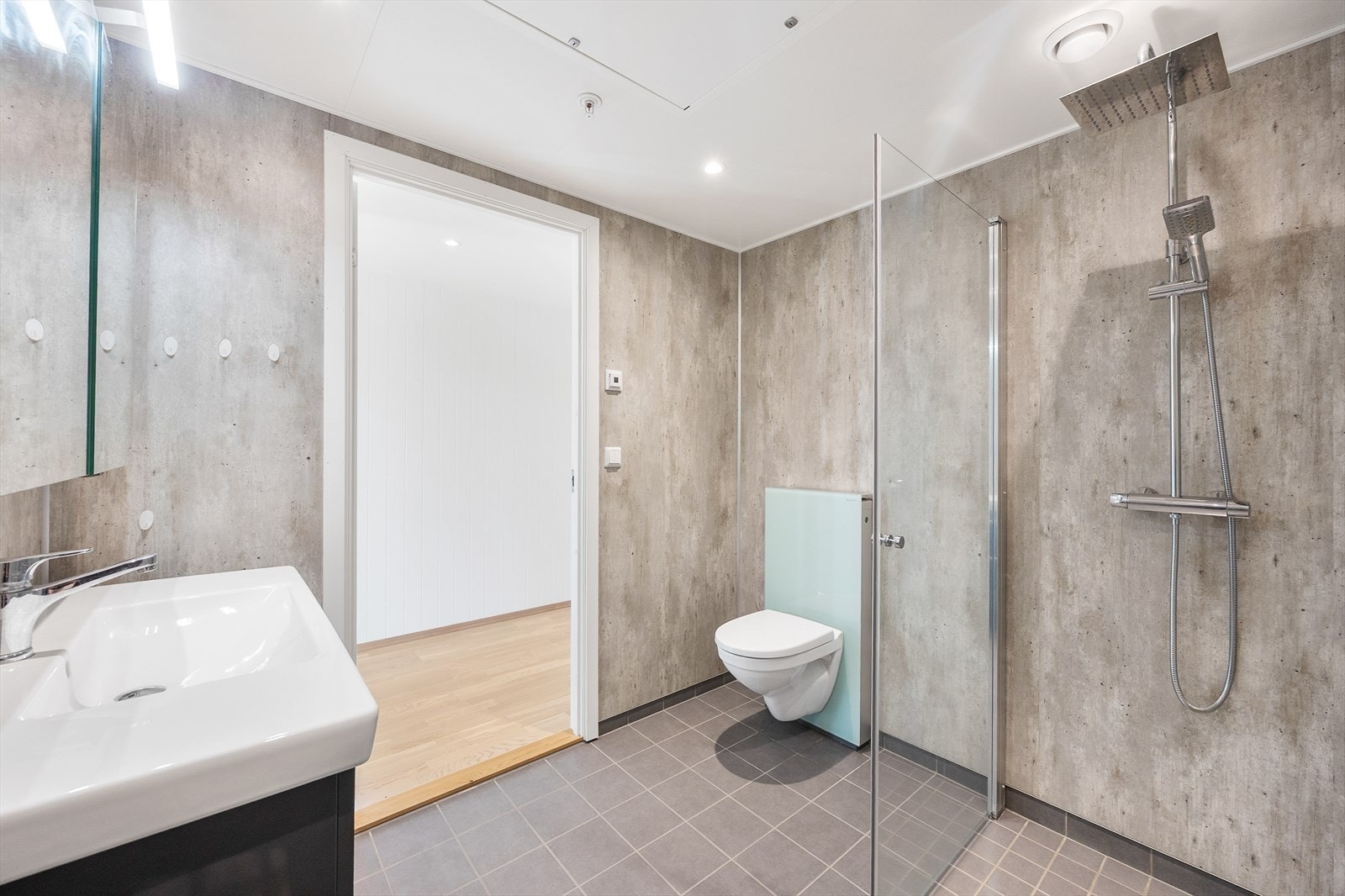 Badet er utstyrt med vegghengt toalett, servant med skuffer og dusjnisje med innfellbare glassdører. Galleribilde