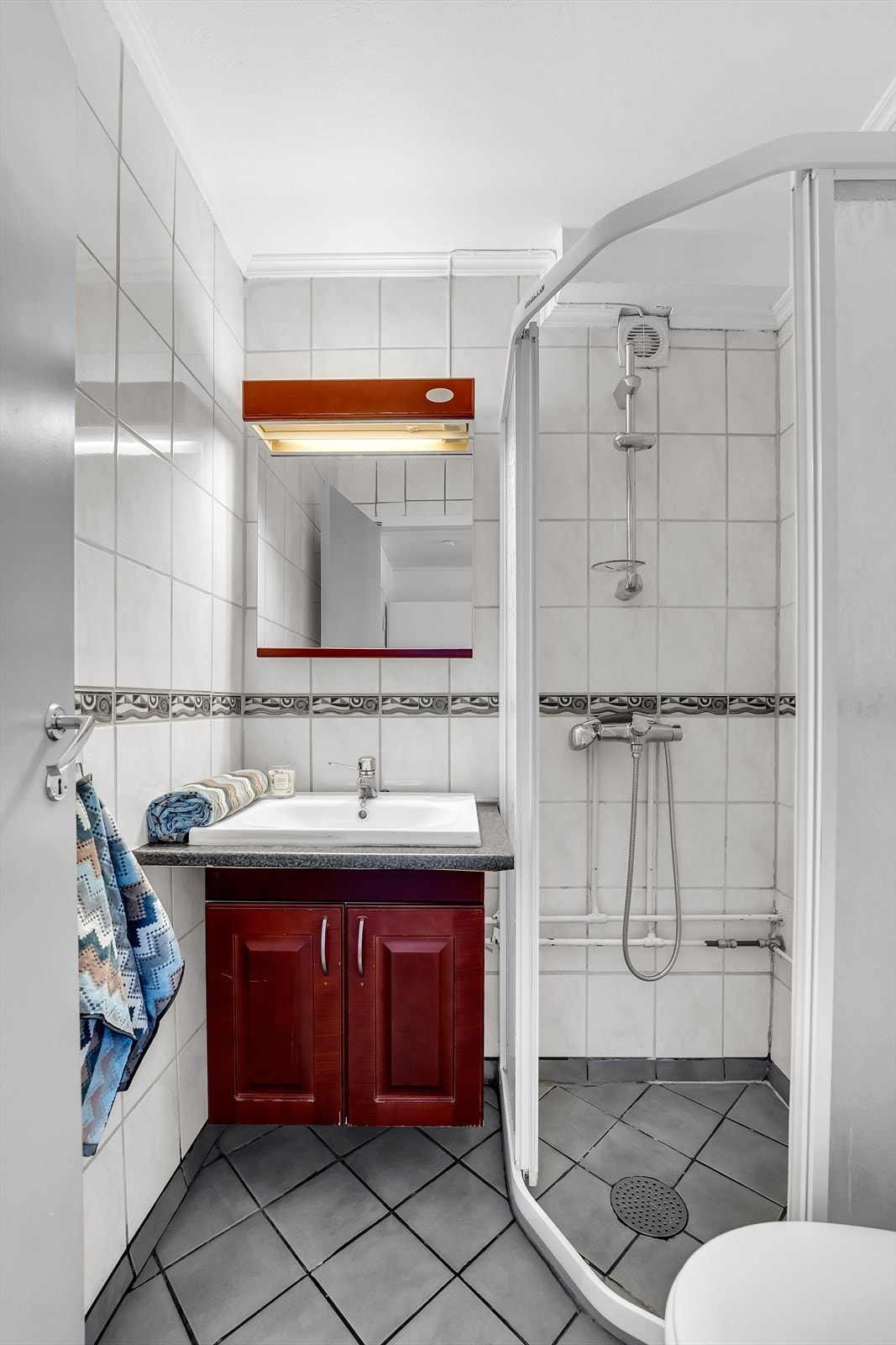 Bad med flislagte vegger og gulv. Her er det servantinnredning, dusjhjørne med skyvedører og toalett. Galleribilde