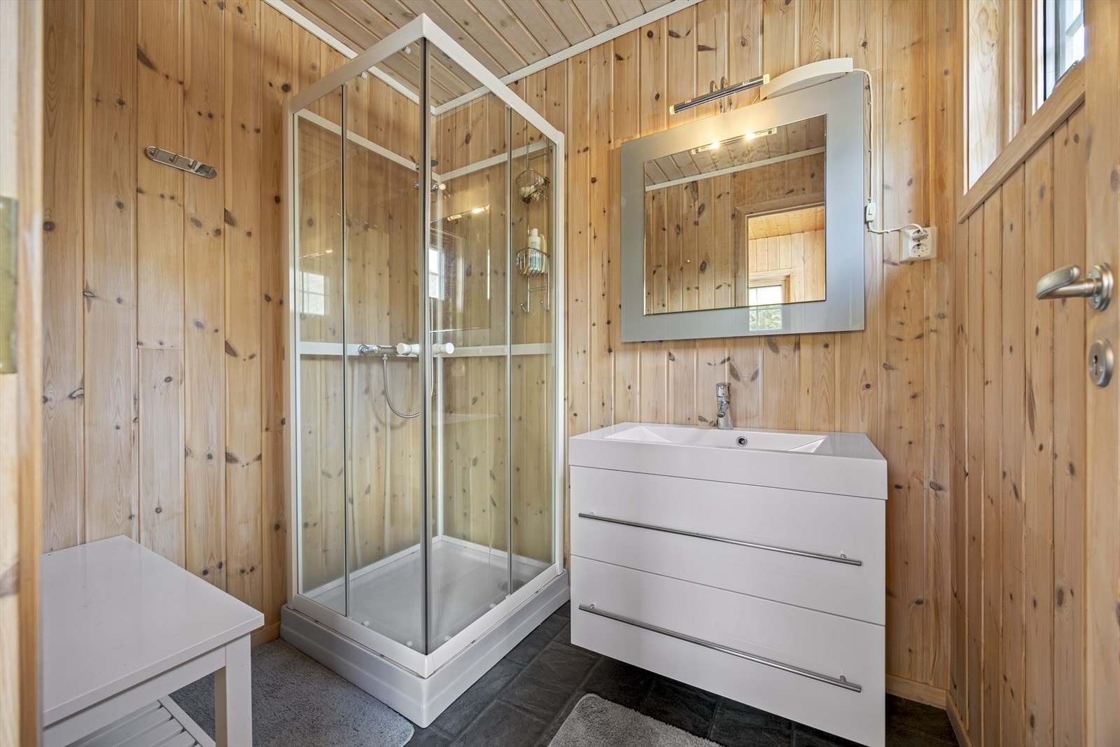 Pent bad med dusjkabinett, servant og moderne innredning. Lyse flater kombinert med treverk gir en lun og innbydende følelse. Galleribilde