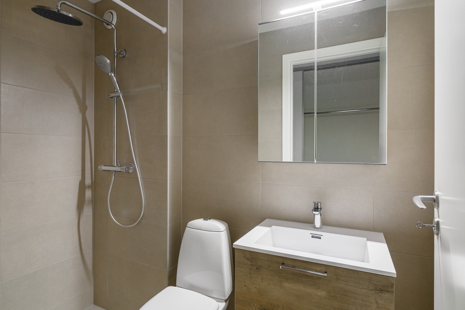 Stilren innredning med servantskap i treverk og speilskap med belysning. Galleribilde