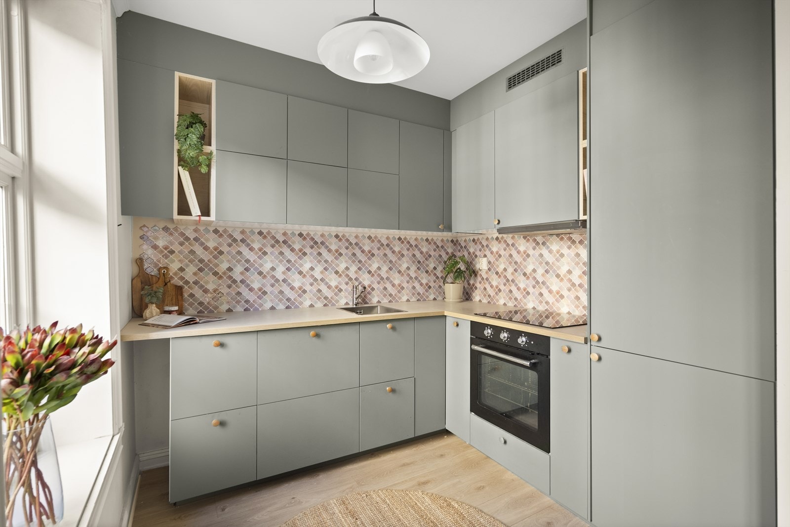 Stilig innredning fra Ikea med grønne, glatte fronter, fliser på vegg over kjøkkenbenk og benkeplate i laminat. Hvitevarene er integrerte, som gir et sømløst helhetsinntrykk. Hvitevarene består av kjøl/frys, oppvaskmaskin, ovn og platetopp. Galleribilde