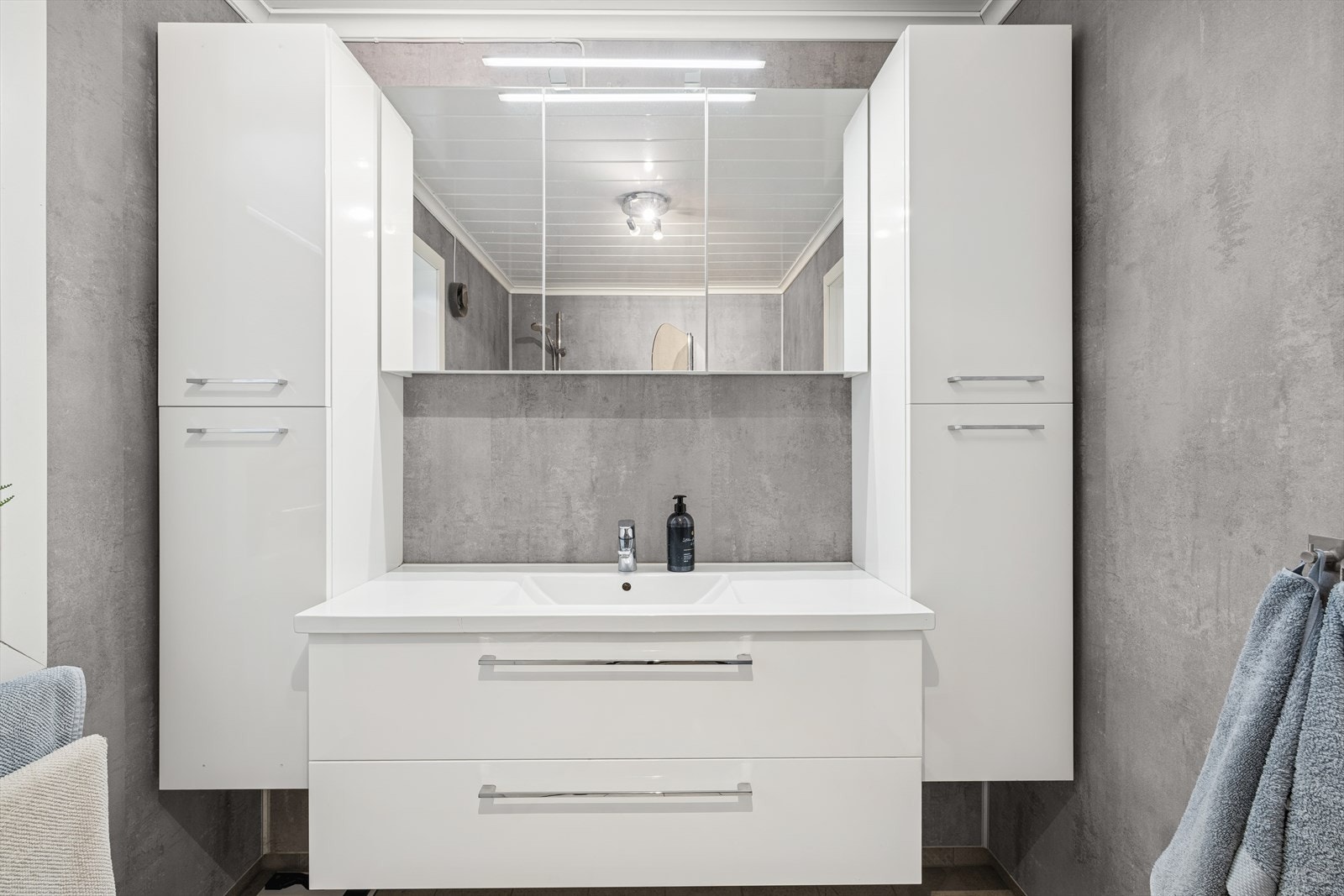 Stilrent uttrykk med flislagte overflater, servant med speil og praktisk høyskap. Galleribilde