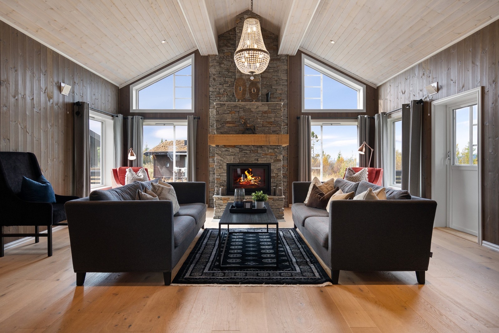 Lys og romslig stue med åpen himling, store vindusflater og peis som gir en lun atmosfære. Galleribilde