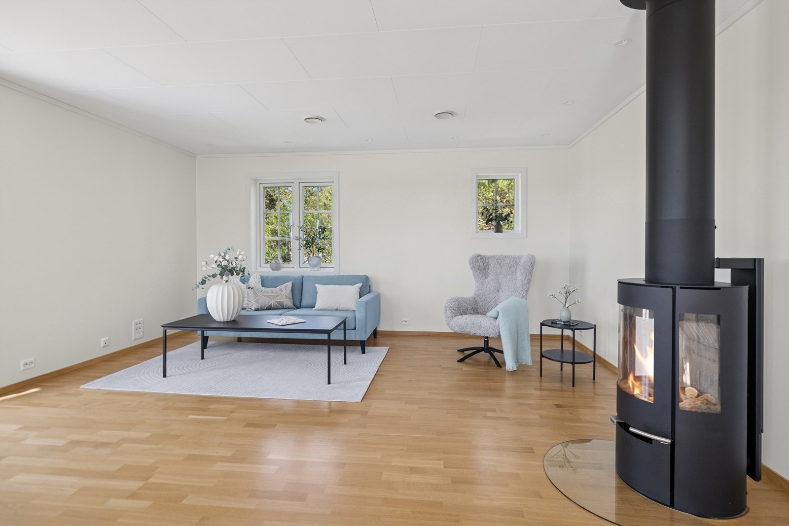 Stuen sett i helhet - med peis, sofadel og vinduer som rammer inn det grønne rundt. En perfekt kombinasjon av funksjonalitet og ro..jpg Galleribilde