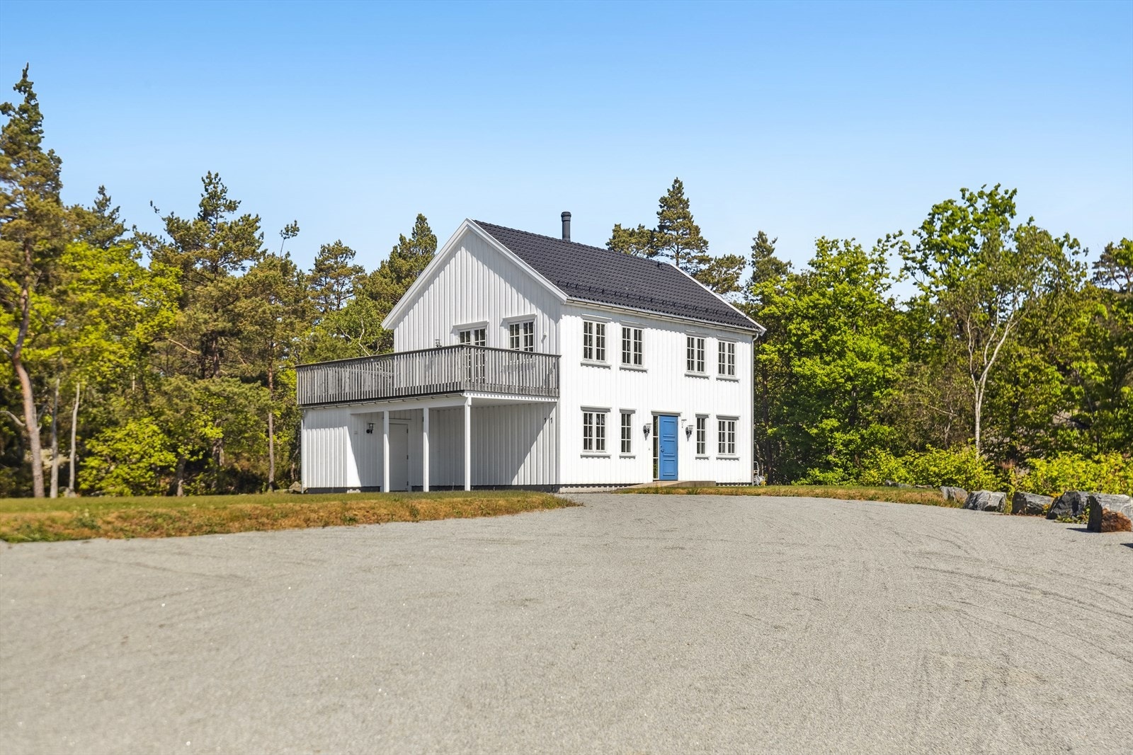 Romslig gruset gårdsplass med god plass til parkering. Boligen har en skjermet beliggenhet omgitt av trær og natur, med veranda i 2. etasje og carport i front. Galleribilde
