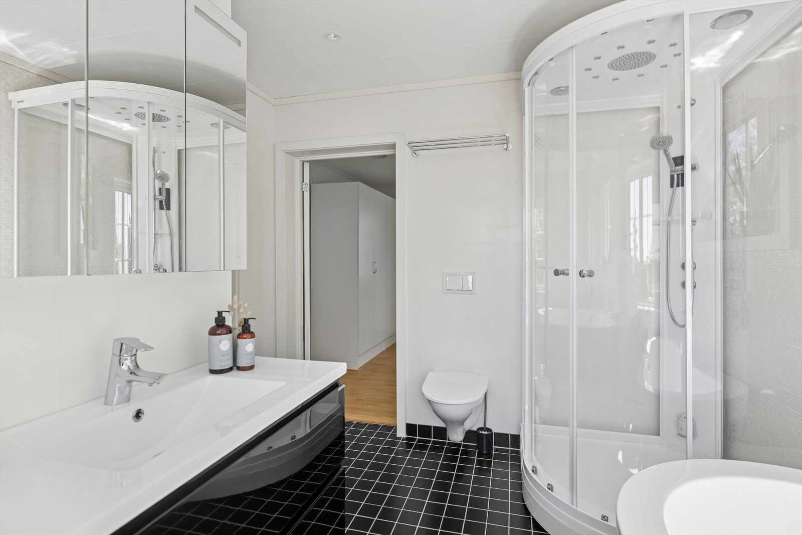 Badet har dusjkabinett med massasjefunksjon, vegghengt toalett og stilren innredning - alt pent integrert i et funksjonelt rom. Galleribilde