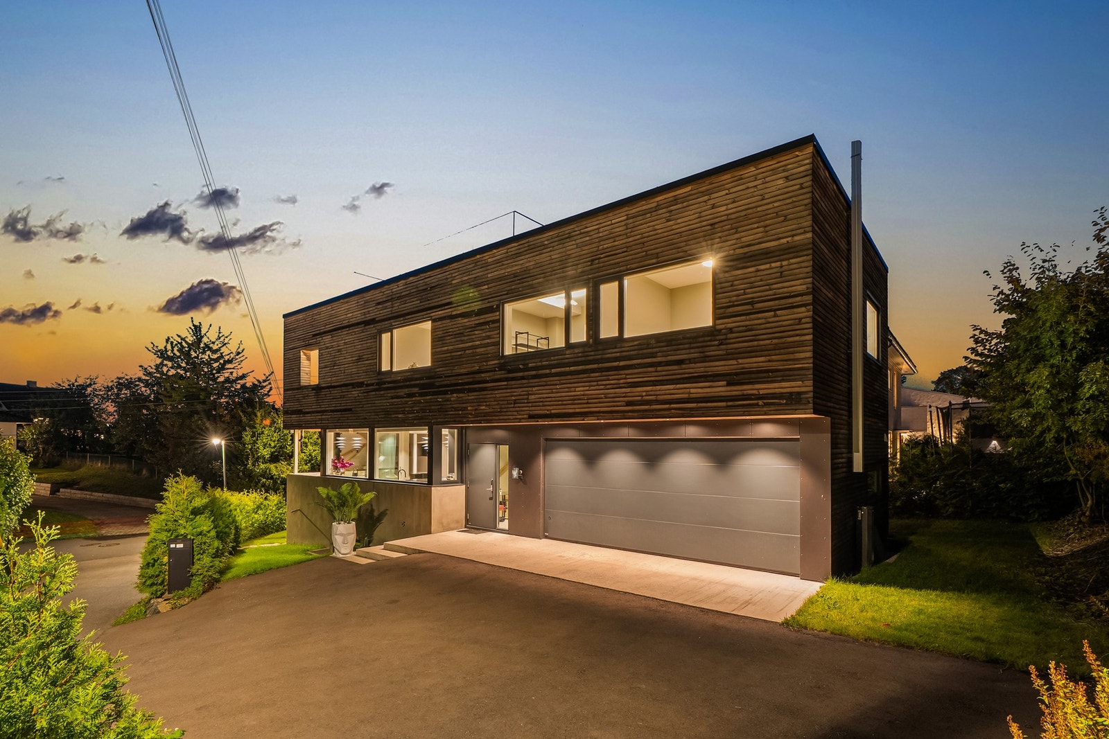 Boligen tar seg vakkert ut i kveldslyset - store vindusflater, varme materialer og diskret utvendig belysning fremhever det moderne uttrykket.