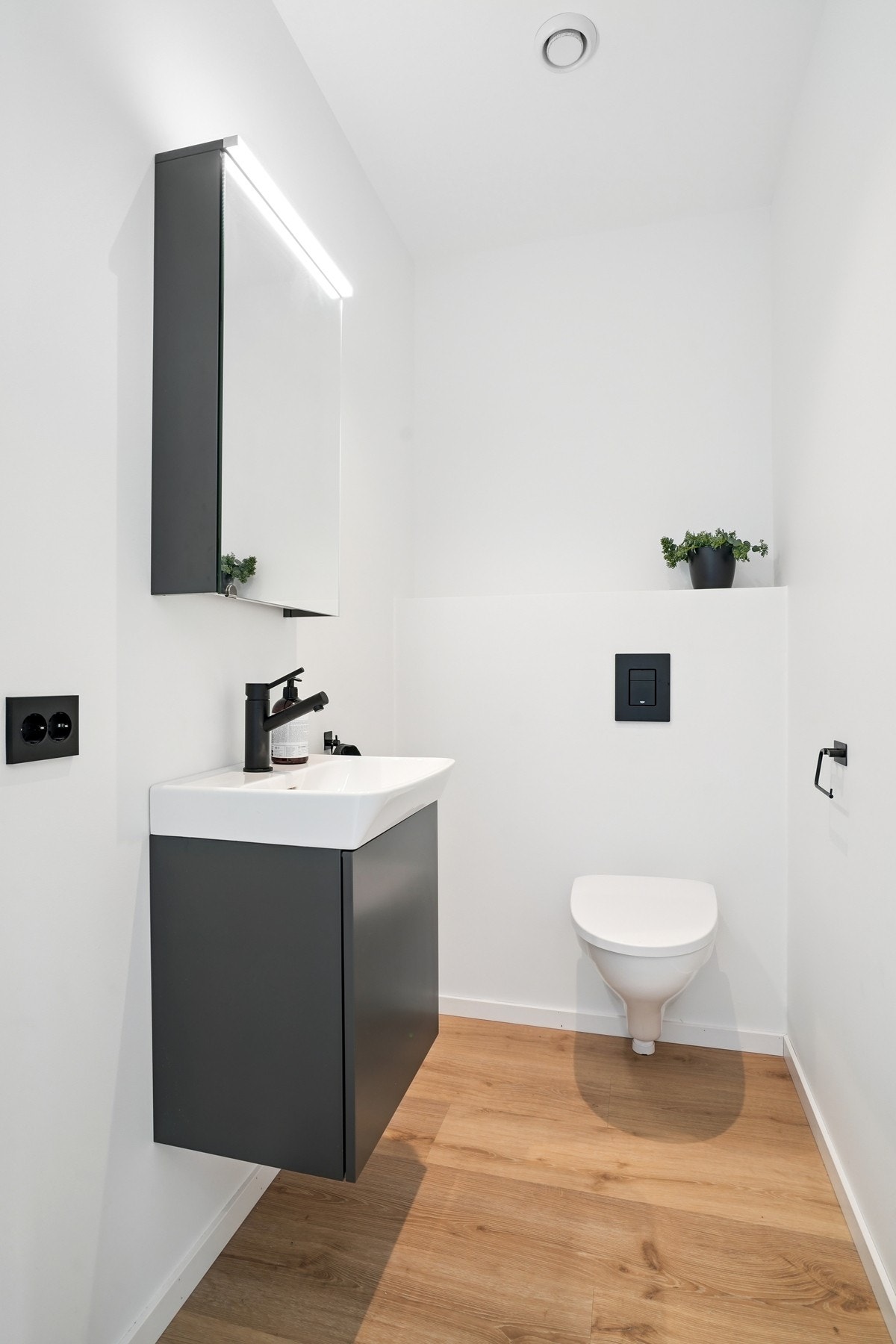 Praktisk toalettrom med gulvflater belagt med vinyl. Innredet med servantinnredning, speilskap med belysning over og vegghengt toalett. Galleribilde