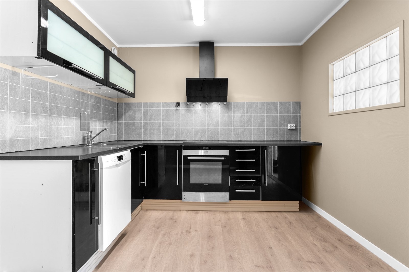 Kjøkkeninnredning med sorte, høyglans skapfronter, laminat benkeplate med fliser på bakvegg. Galleribilde