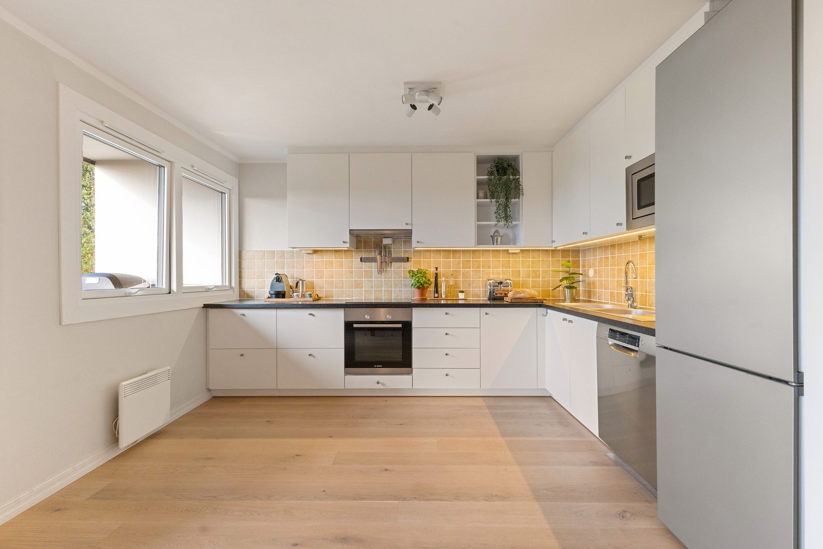 tilren kjøkkeninnredning fra 2013, utført med slette fronter, et åpent overskap og benkeplate av laminat med nedfelt benkebeslag med dobbel oppvaskkum. Galleribilde