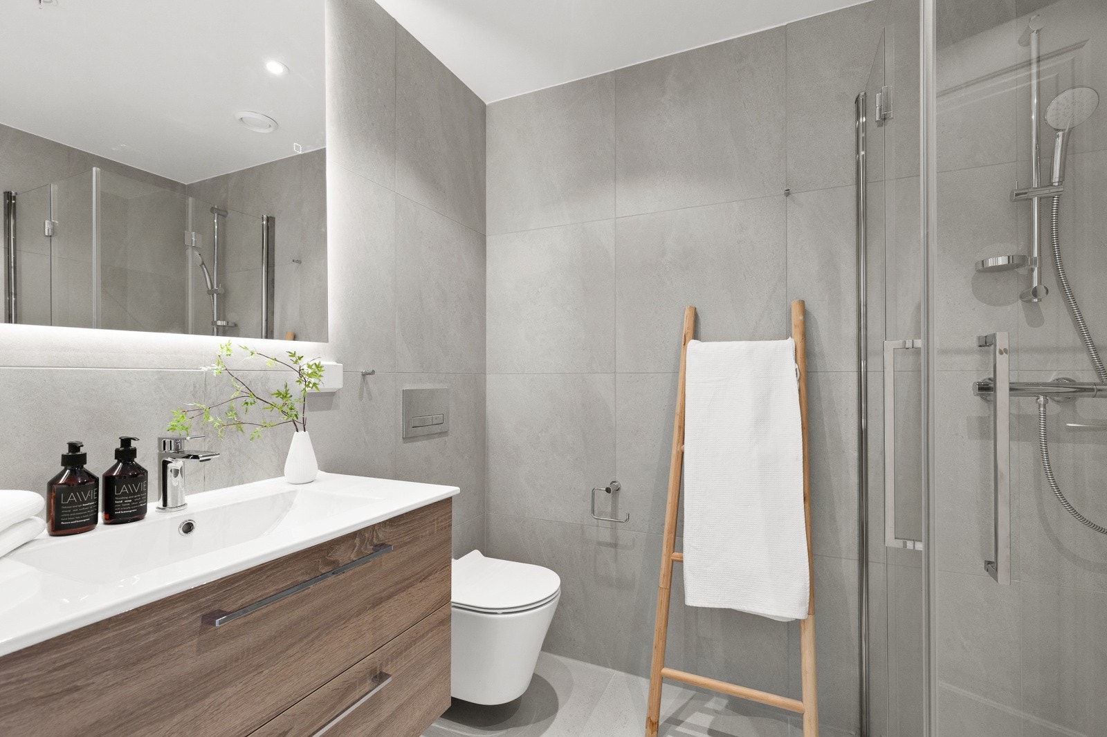 Lekkert baderom utstyrt med downlights, varmekabler, vegghengt toalett, dusjhjørne og servant samt speil. Galleribilde