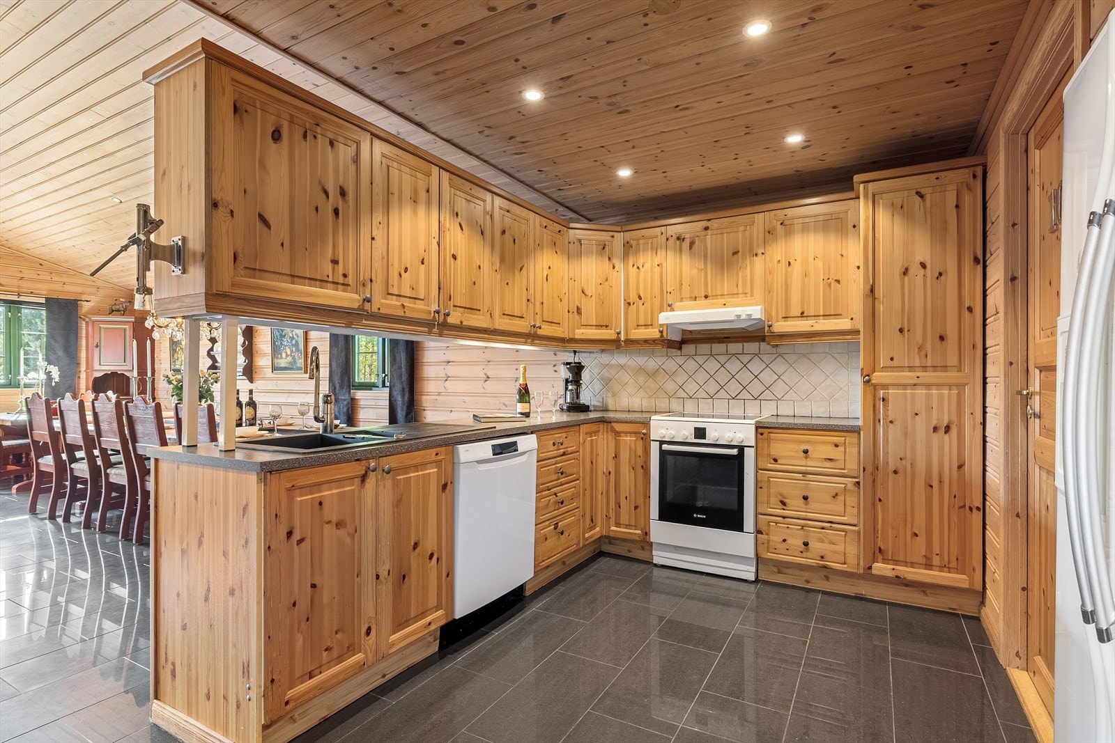 Kjøkkenet har en romslig kjøkkeninnredning i furu med oppvaskmaskin, komfyr og side- by side kjøl- og fryseskap. Galleribilde