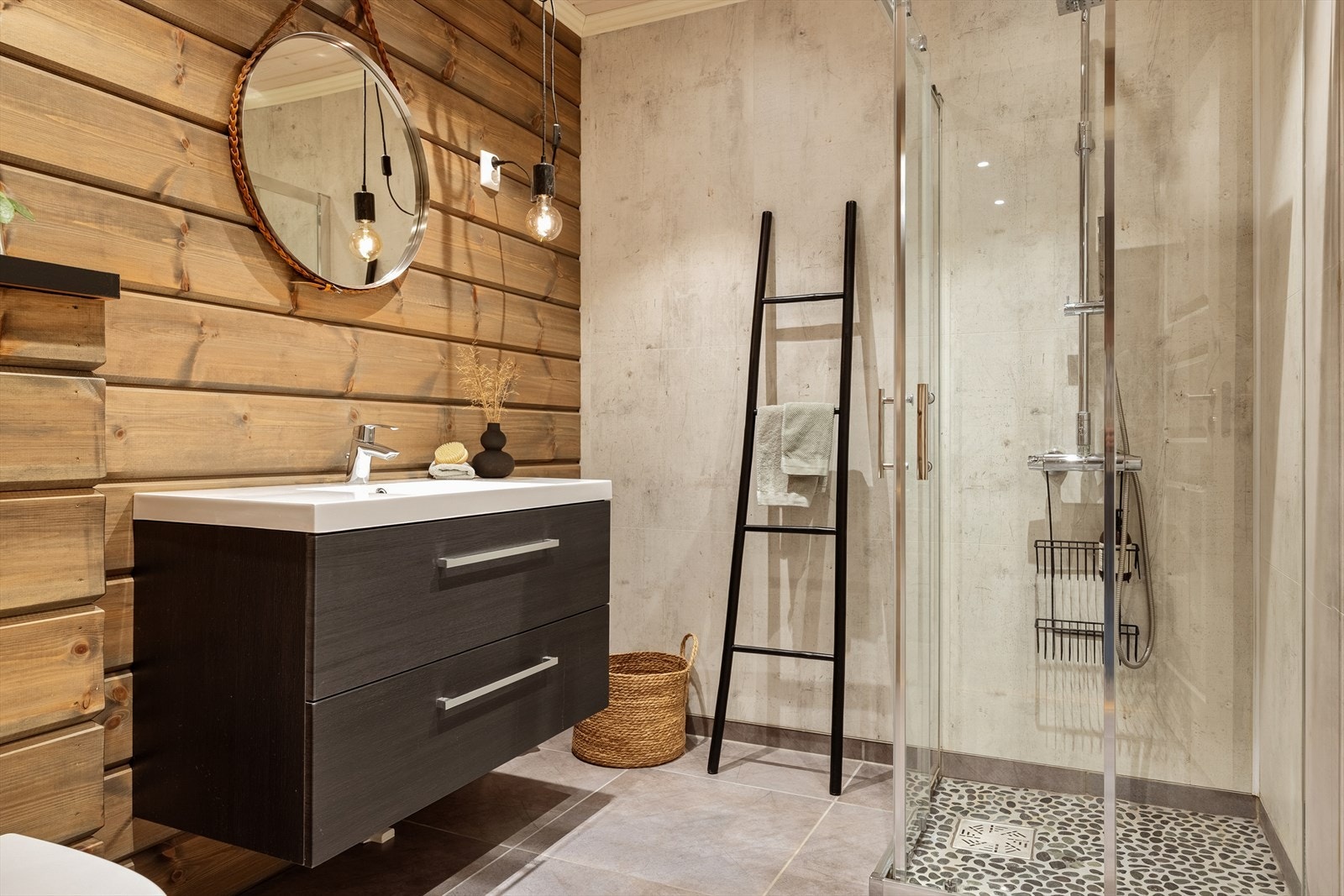 Badet er romslig og inneholder vegghengt toalett, helstøpt servant, skuffer under servant med slette fronter og dusjdører i klart glass Galleribilde