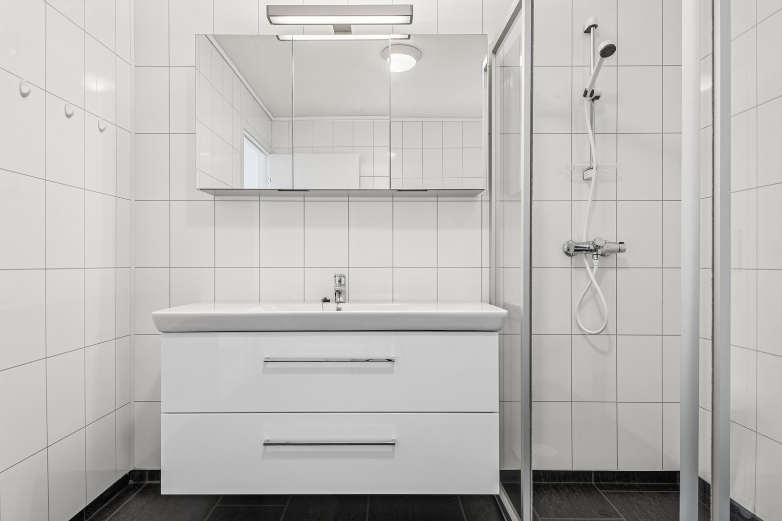 Badet er innredet med vegghengt toalett, dusjhjørne, opplegg for vaskemaskin og innredning med servant. Galleribilde