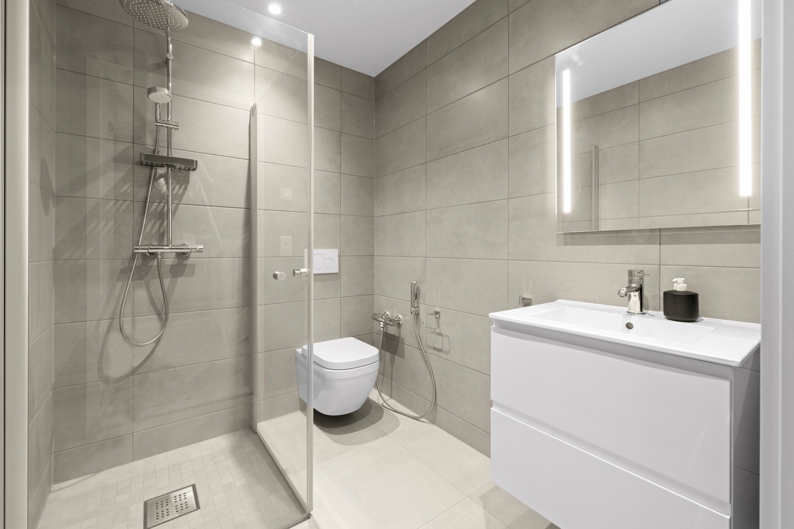 Hovedbadet ligger i 1. etasje og holder en moderne standard med flislagte overflater, vegghengt toalett, dusjhjørne og innredning med nedfelt servant. Galleribilde