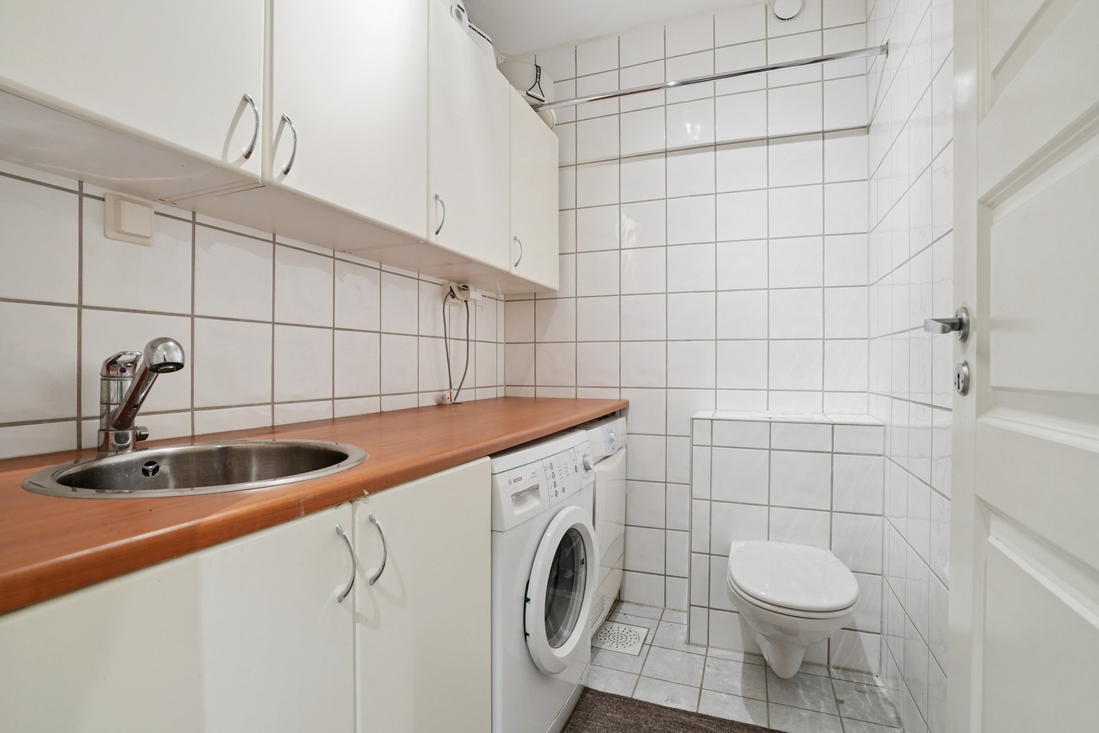 Separat vaskerom med fliser på vegger og gulv, samt varmekabler i gulvet. Innredet med vegghengt toalett, innredning med nedfelt stålkum, laminat benkeplate og opplegg for vaskemaskin. Galleribilde