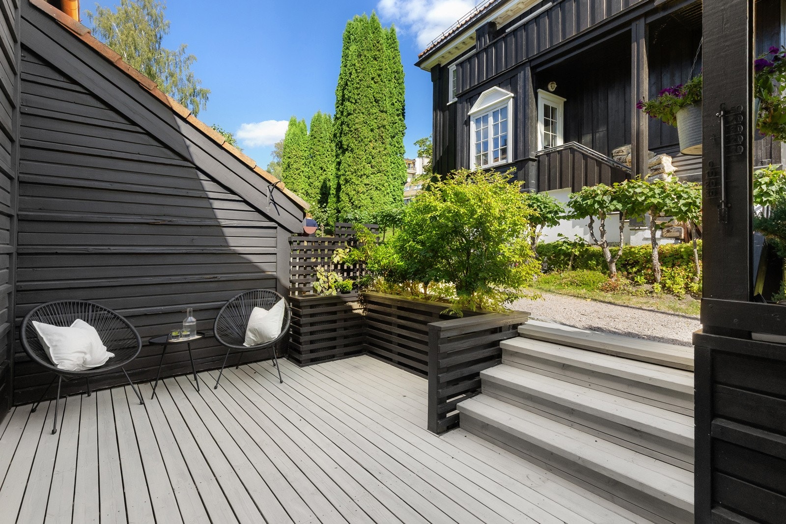 Terrassen har en fin størrelse, dekke av terrassebord, overbygg ved ytterdøren, rekkverk med blomsterkasse og levegg i enden. Her er det også inngang til en utebod. Galleribilde