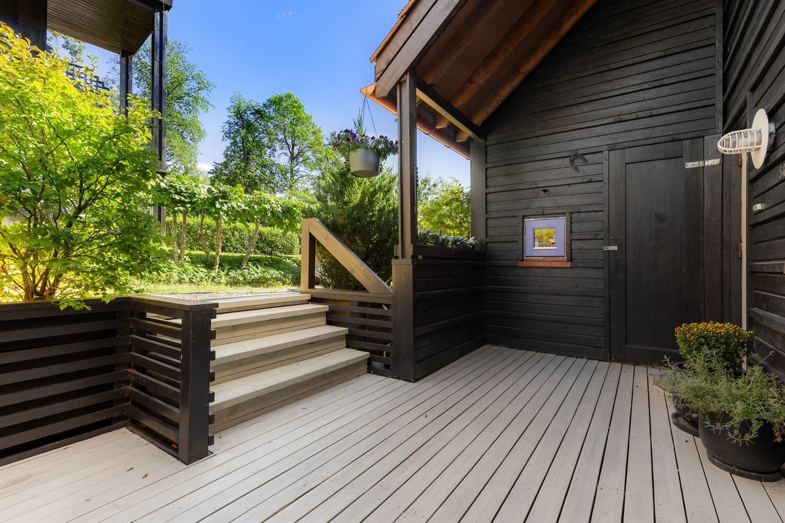 Terrassen har en fin størrelse, dekke av terrassebord, overbygg ved ytterdøren, rekkverk med blomsterkasse og levegg i enden. Her er det også inngang til en utebod. Galleribilde
