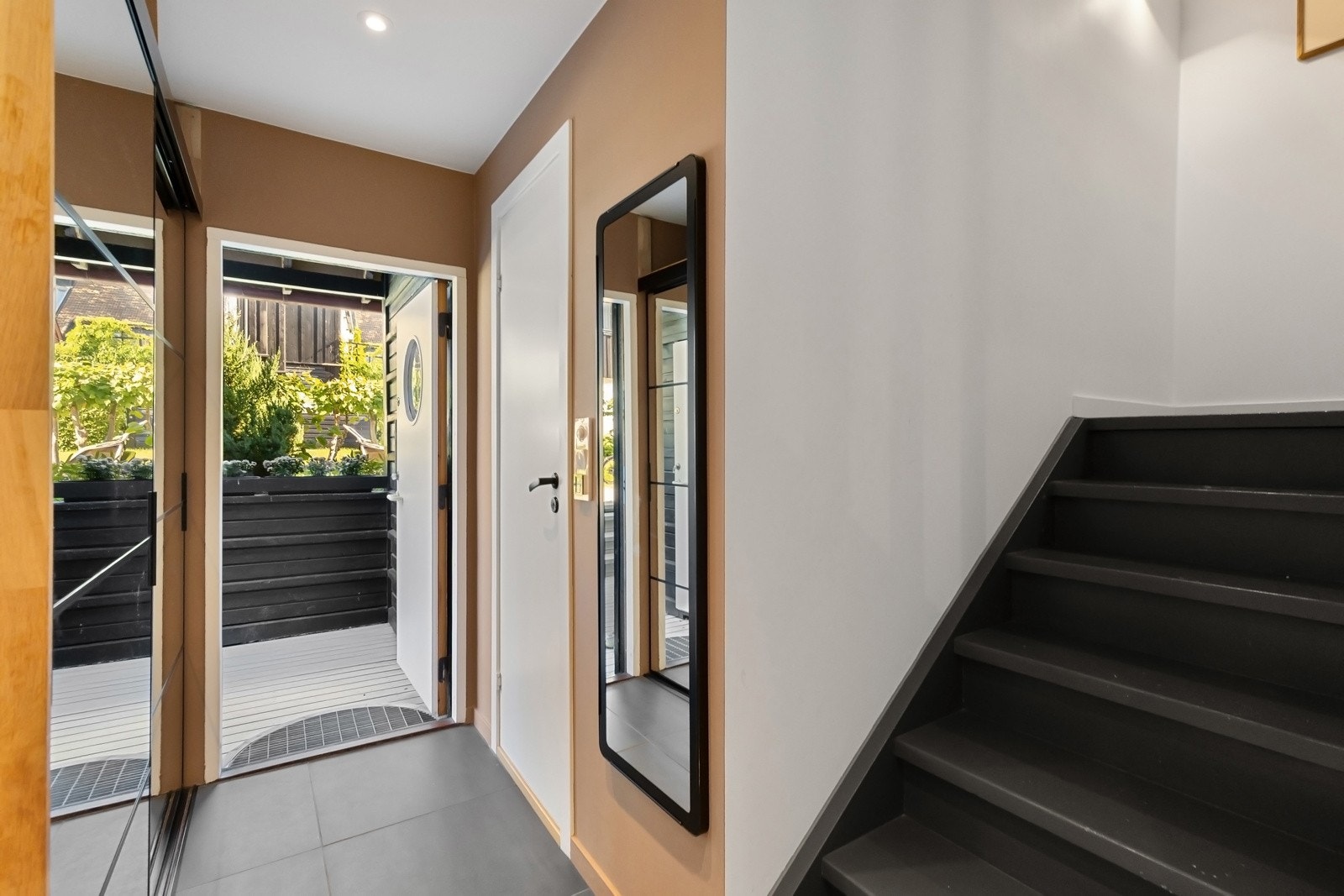 Entreen er innbydende med gulvvarme under mørke gulvfliser i storformat, glatte veggflater malt i en varm terrakottafarge og listefri, hvitmalt himling med downlights. Galleribilde