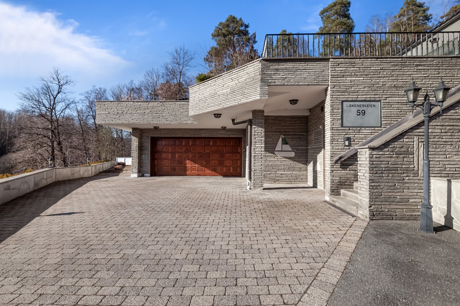 Boligen har dobbelgarasje med lader for elbil og dør inn til boligen. Det er også stor gårdsplass med plass til ytterligere flere biler. Porten inn til gårdsplassen kan åpnes via porttelefon på kjøkkenet. Galleribilde