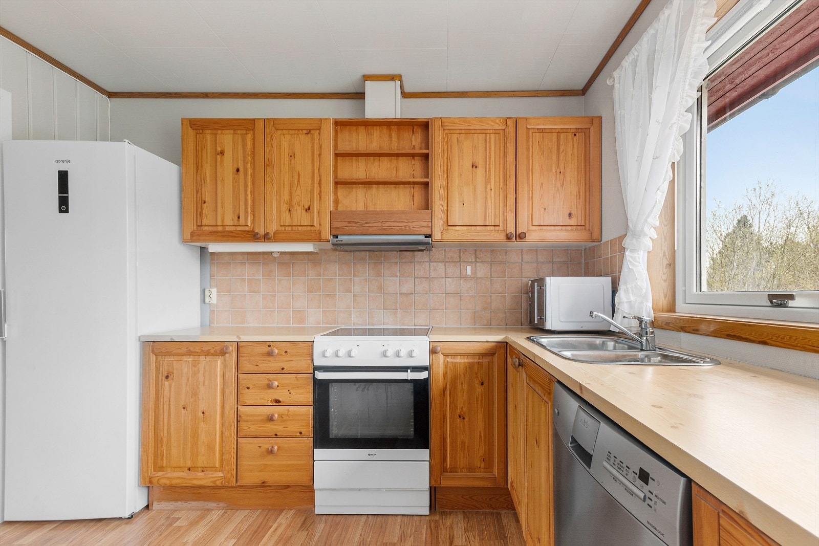 Kjøkkenet er innredet med frittstående kjøl/fryseskap, oppvaskmaskin, komfyr og mikro. Galleribilde