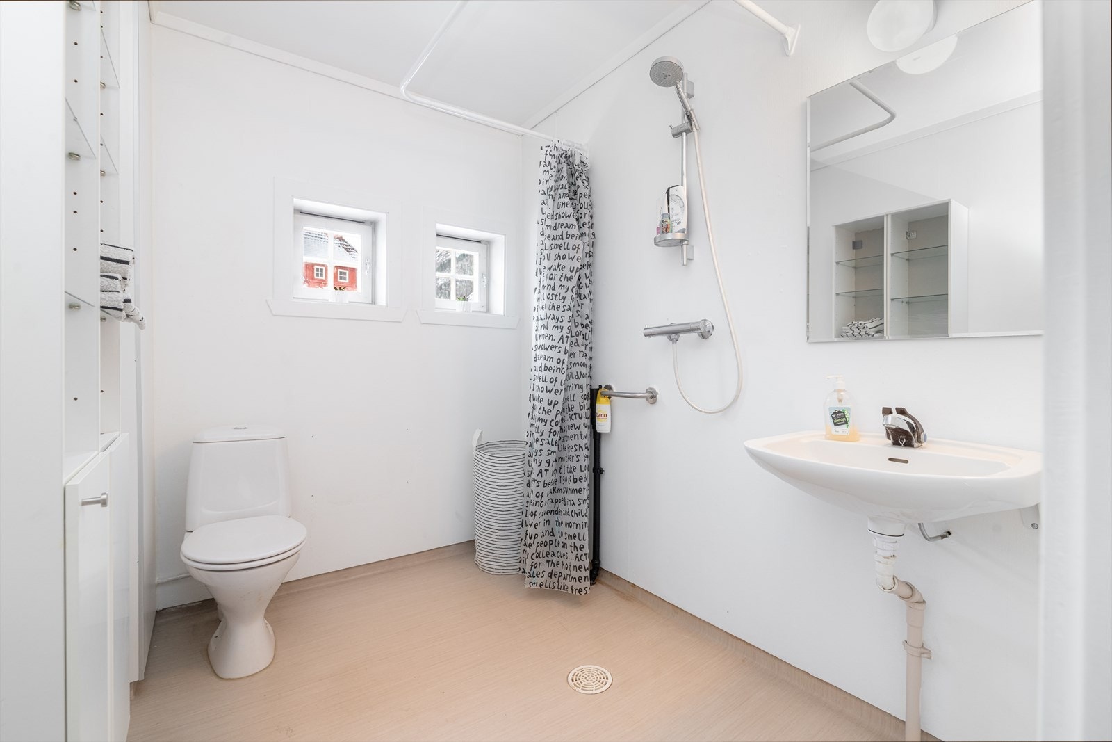 Badet er innredet med toalett, servant på vegg og vegghengt dusj med forheng. Det er panelovn på vegg. Galleribilde