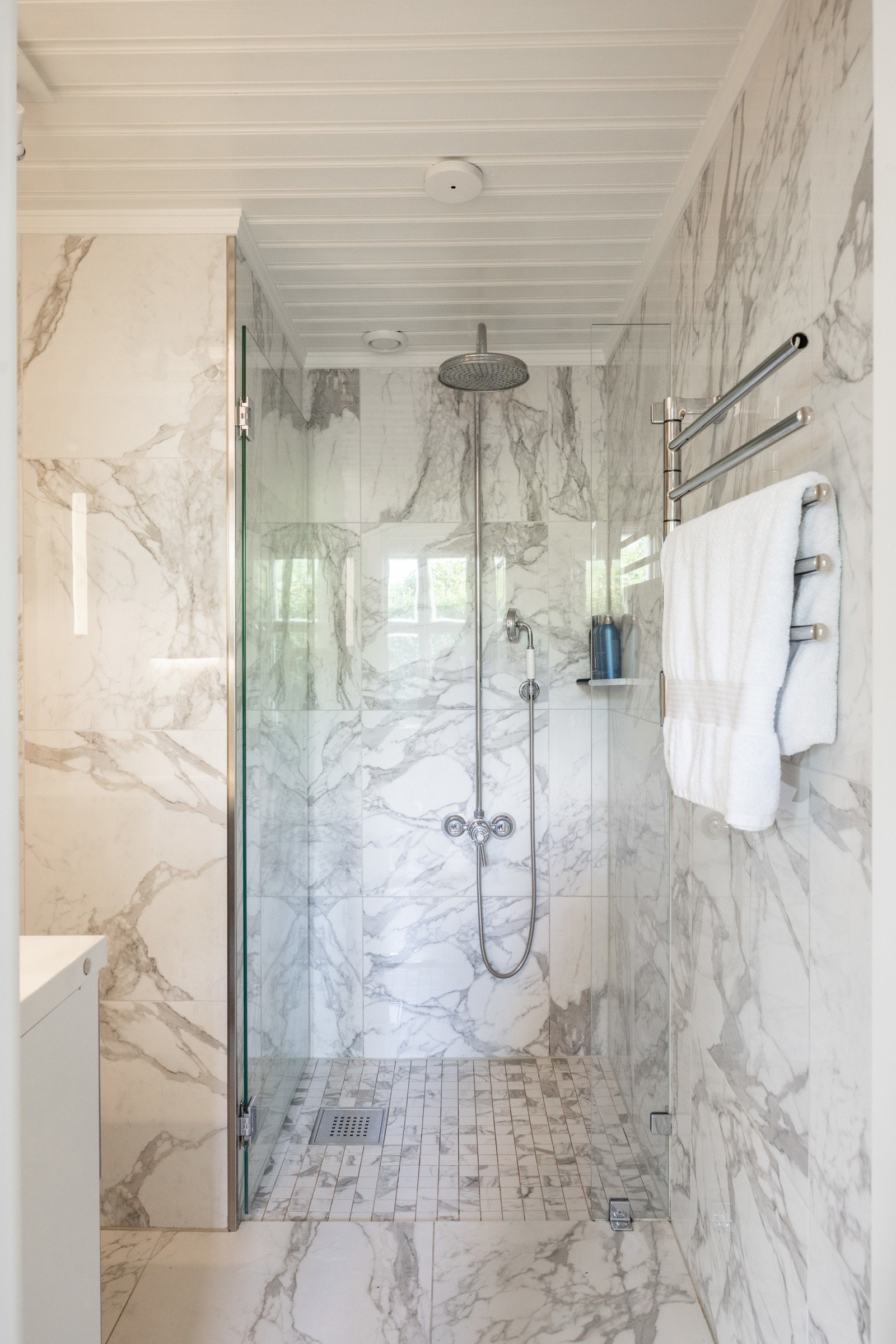 Badet er stilfullt innredet med fliser i marmorlook, dusjhjørne med glassvegg, moderne servantinnredning og håndkletørker. Galleribilde