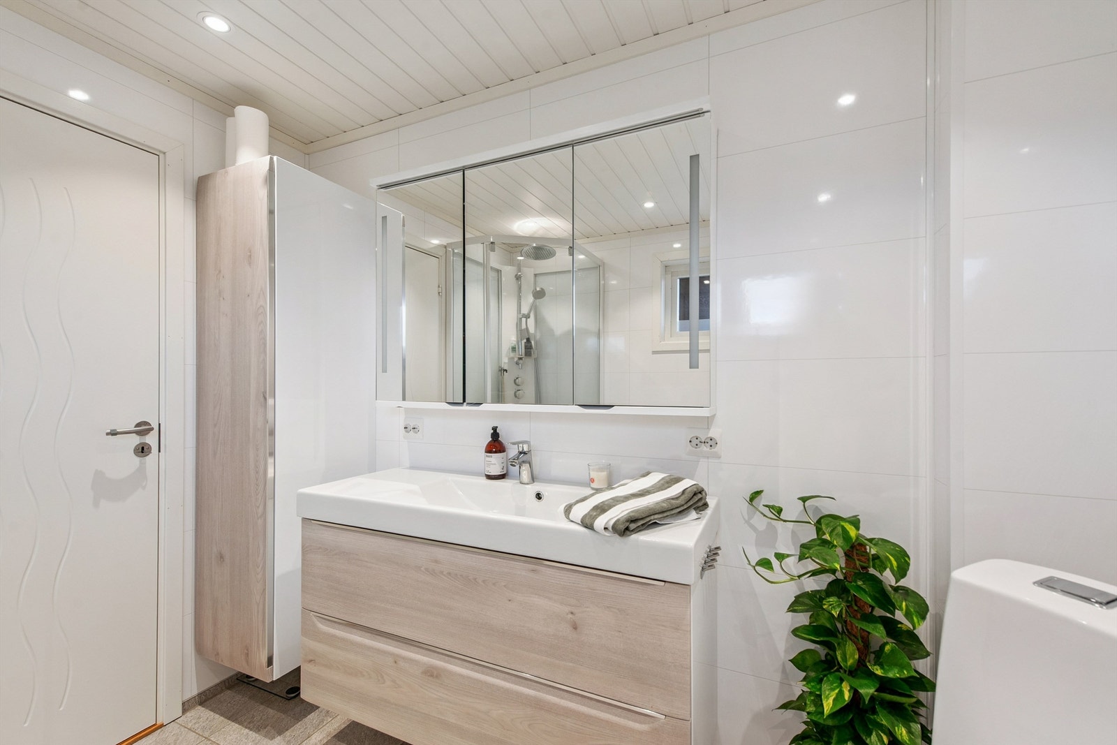 Moderne baderomsinnredning med skuffer, heldekkende servant, speilskap og ekstra høyskap for god oppbevaring. Galleribilde