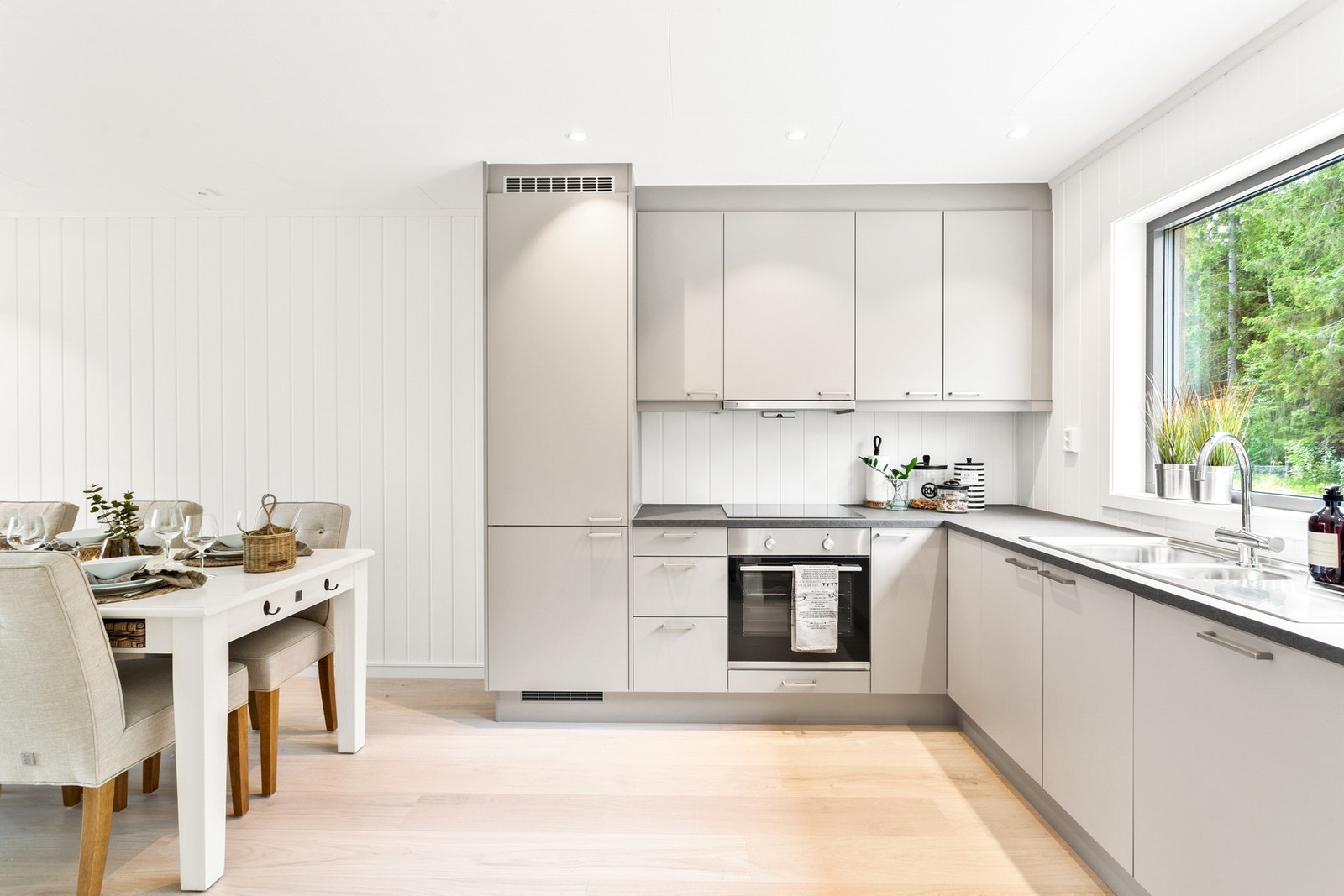 Stilfull kjøkkeninnredning med glatte fronter, benkeplater i laminat, oppvaskkum med ett-greps blandebatteri og ventilator over kokesonen. Galleribilde